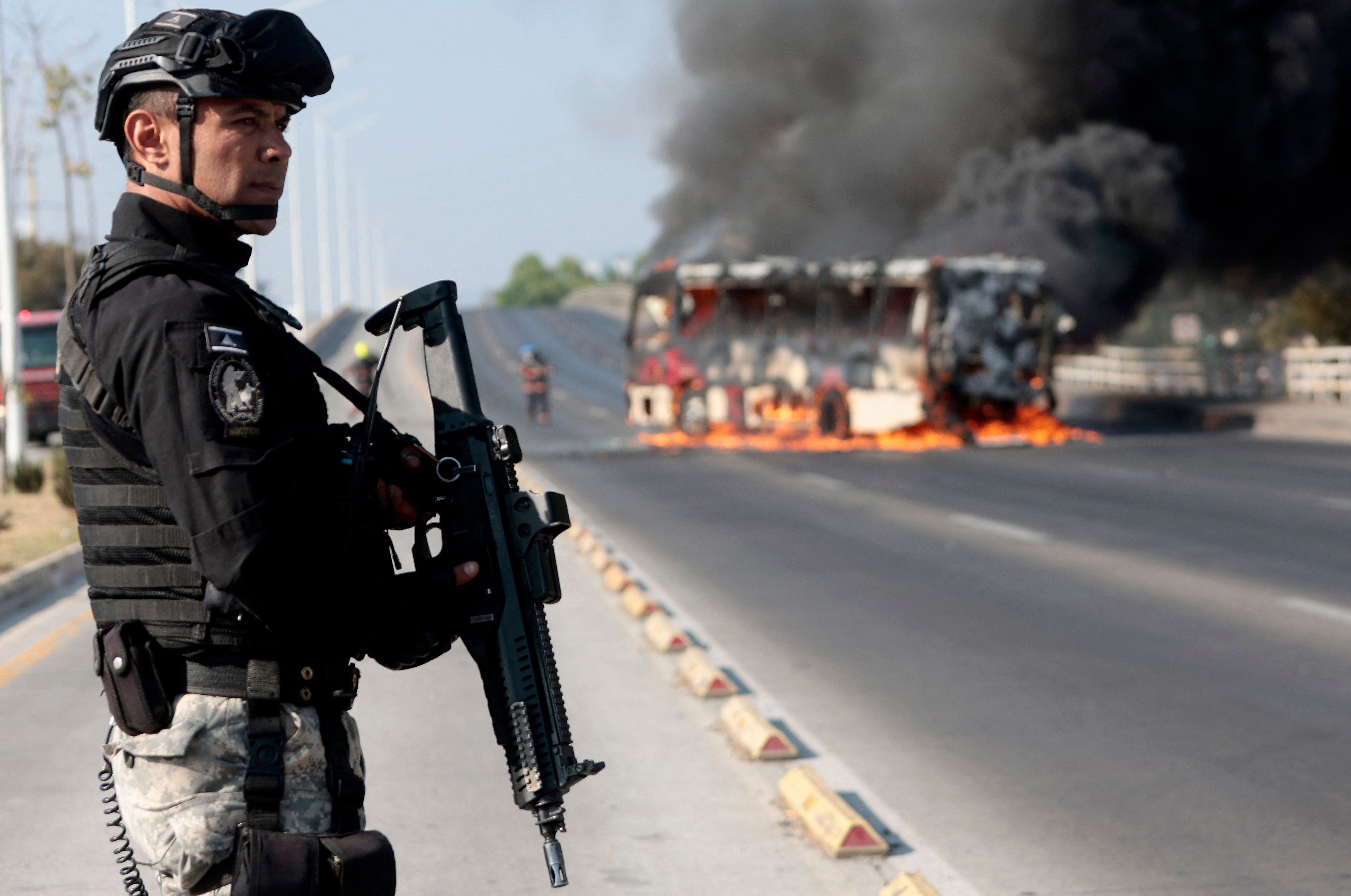 <p>A member of the Prosecutor's Office stands guard near a burning bus at one of the main avenues after it was set on fire by organised crime groups in response to an operation in Jalisco to arrest a high-priority security target in Zapopan, state of Jalisco, Mexico.</p>