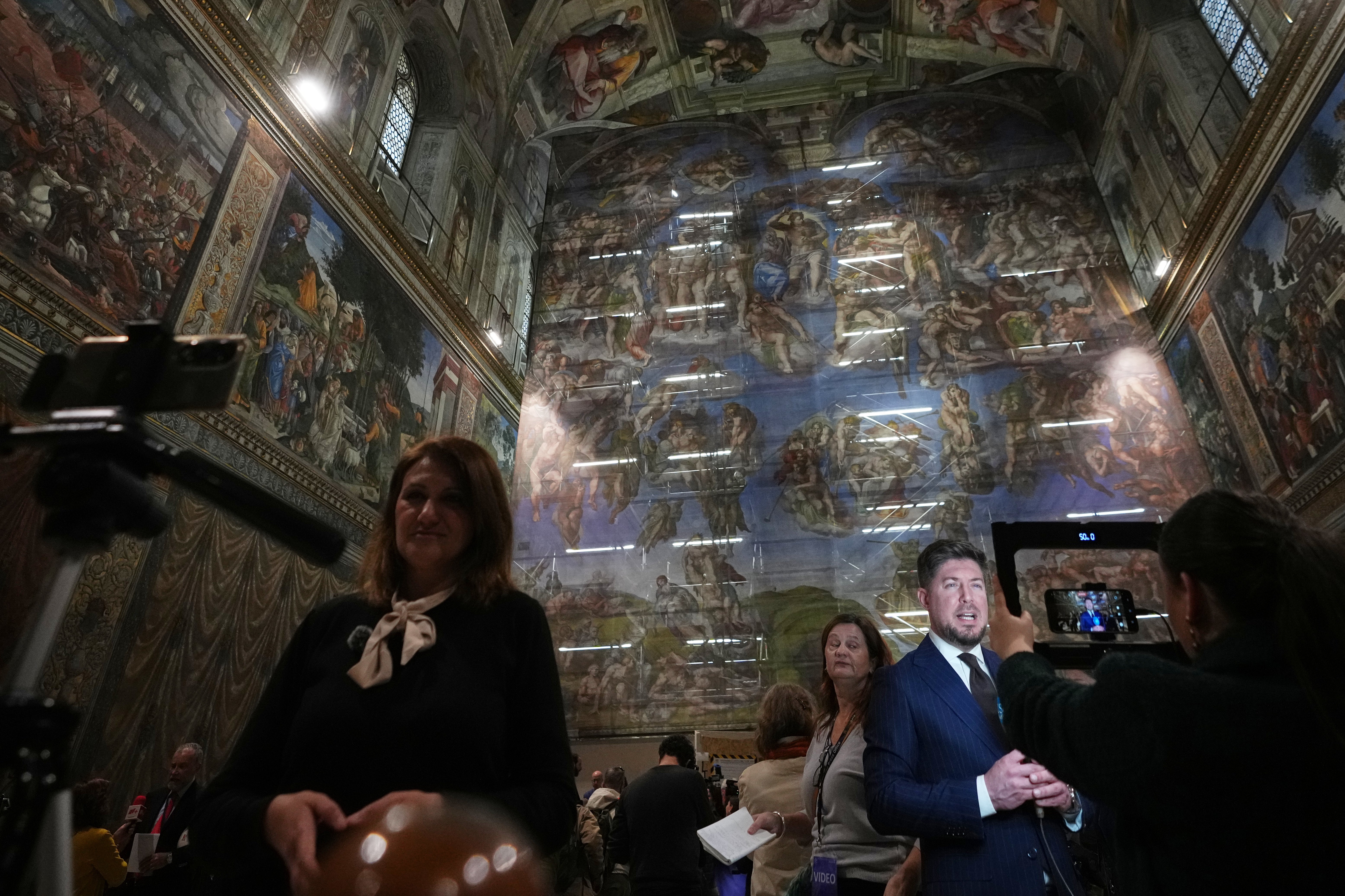Journalists report in front of a screen with a replica of ‘The Last Judgment,’ superimposed on it that covers the scaffolding used for its extraordinary maintenance, during the presentation for press in the Sistine Chapel at the Vatican, Saturday, Feb. 28, 2026. (AP Photo/Alessandra Tarantino)