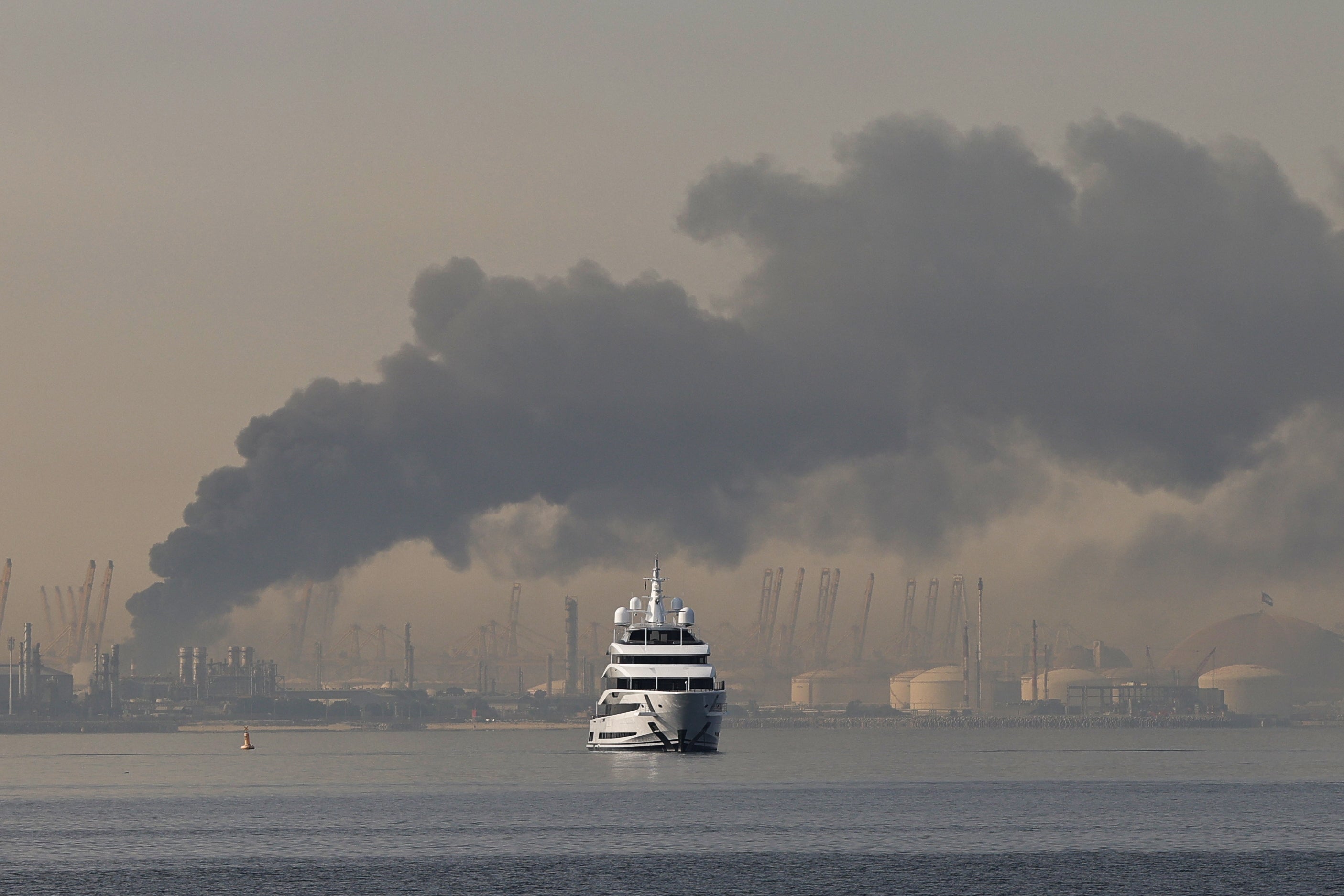 A yacht sails past a plume of smoke rising from the port of Jebel Ali following a reported Iranian strike in Dubai on March 1, 2026.