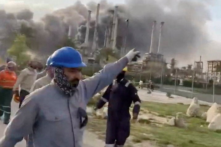 Workers evacuate the area around Saudi Aramco's Ras Tanura oil refinery as smoke rises following a reported Iranian drone strike in Ras Tanura, Saudi Arabia, on Monday
