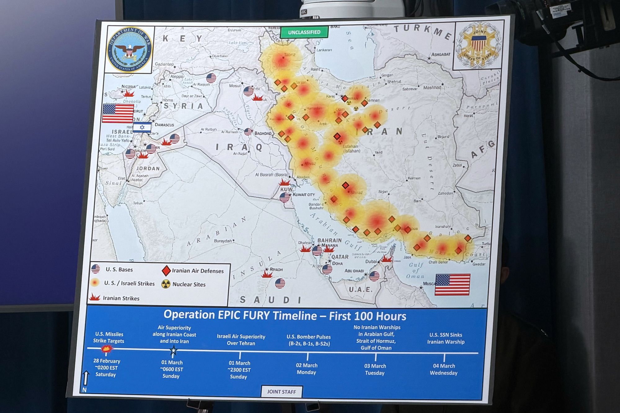 A Department of Defense map titled ‘Operation EPIC FURY Timeline - First 100 Hours’ is displayed during the Pentagon briefing