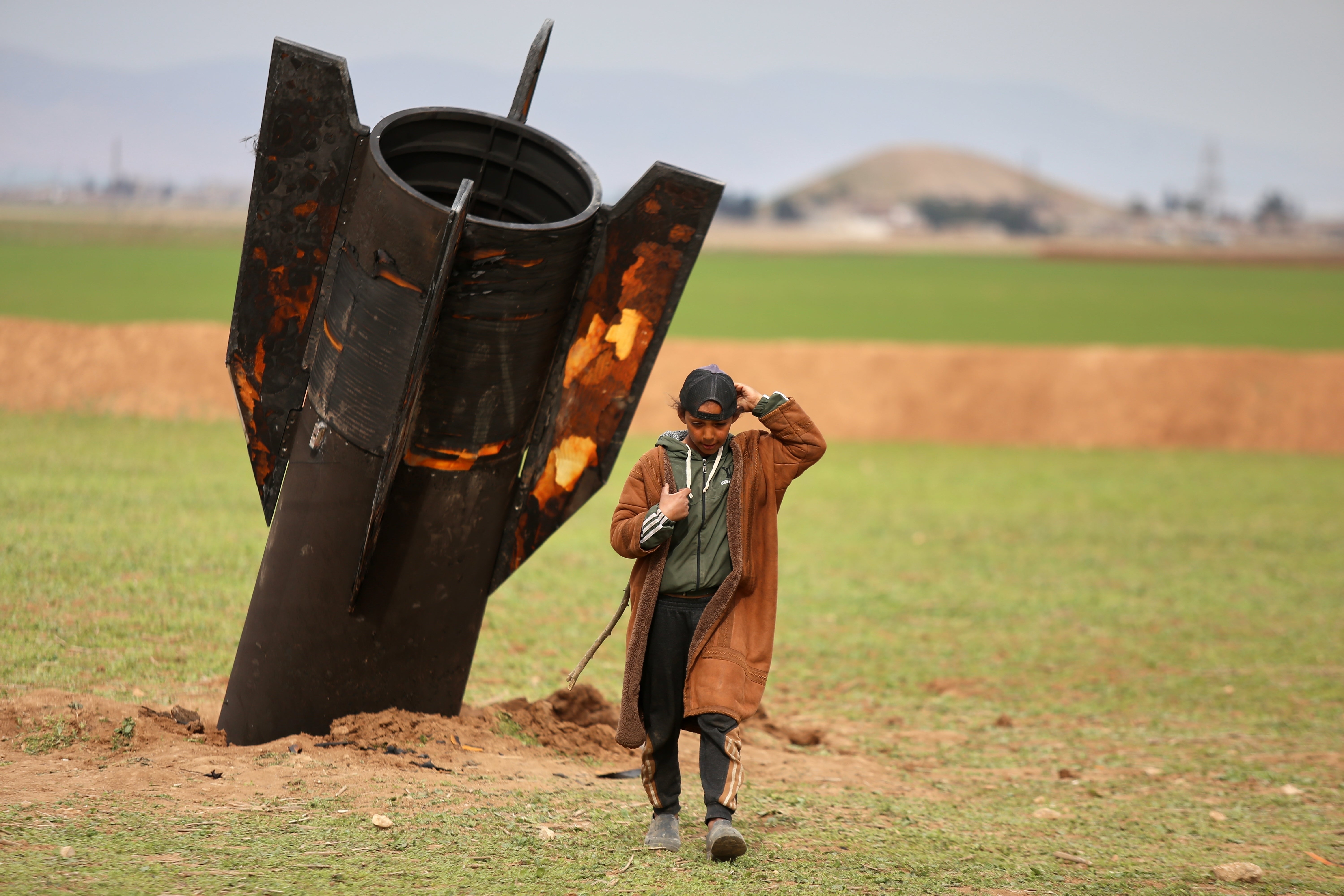 A shepherd boy walks away from an unexploded Iranian shell that landed in an open field on the outskirts of Qamishli in eastern Syria on March 4, 2026.