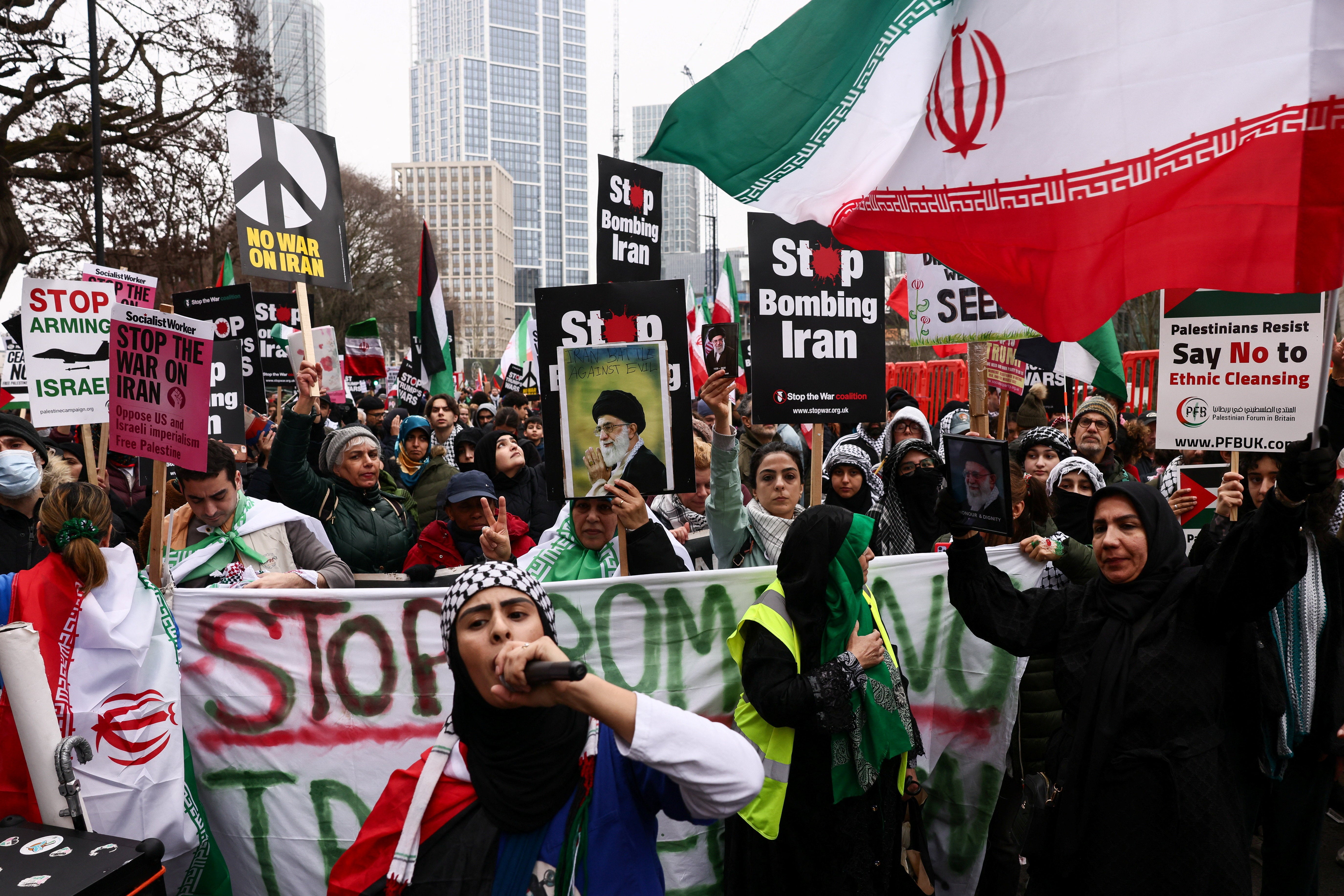 Anti-war activists hold signs, images of Iran's late Supreme Leader Ayatollah Ali Khamenei, and Iranian flags as they gather outside the US embassy