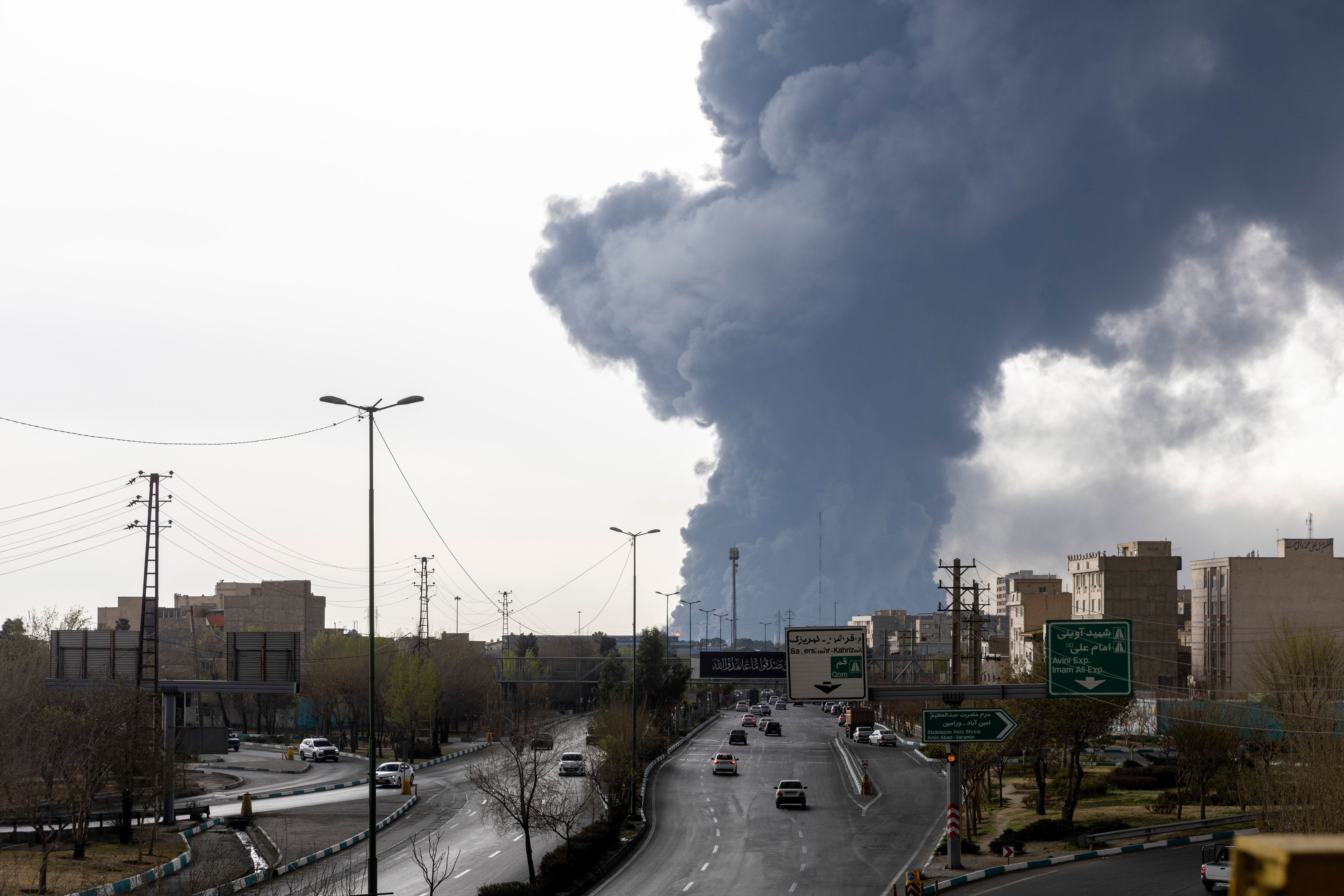 Cars drive down a highway as smoke billows after overnight airstrikes on oil depots on March 8, 2026 in Tehran, Iran.