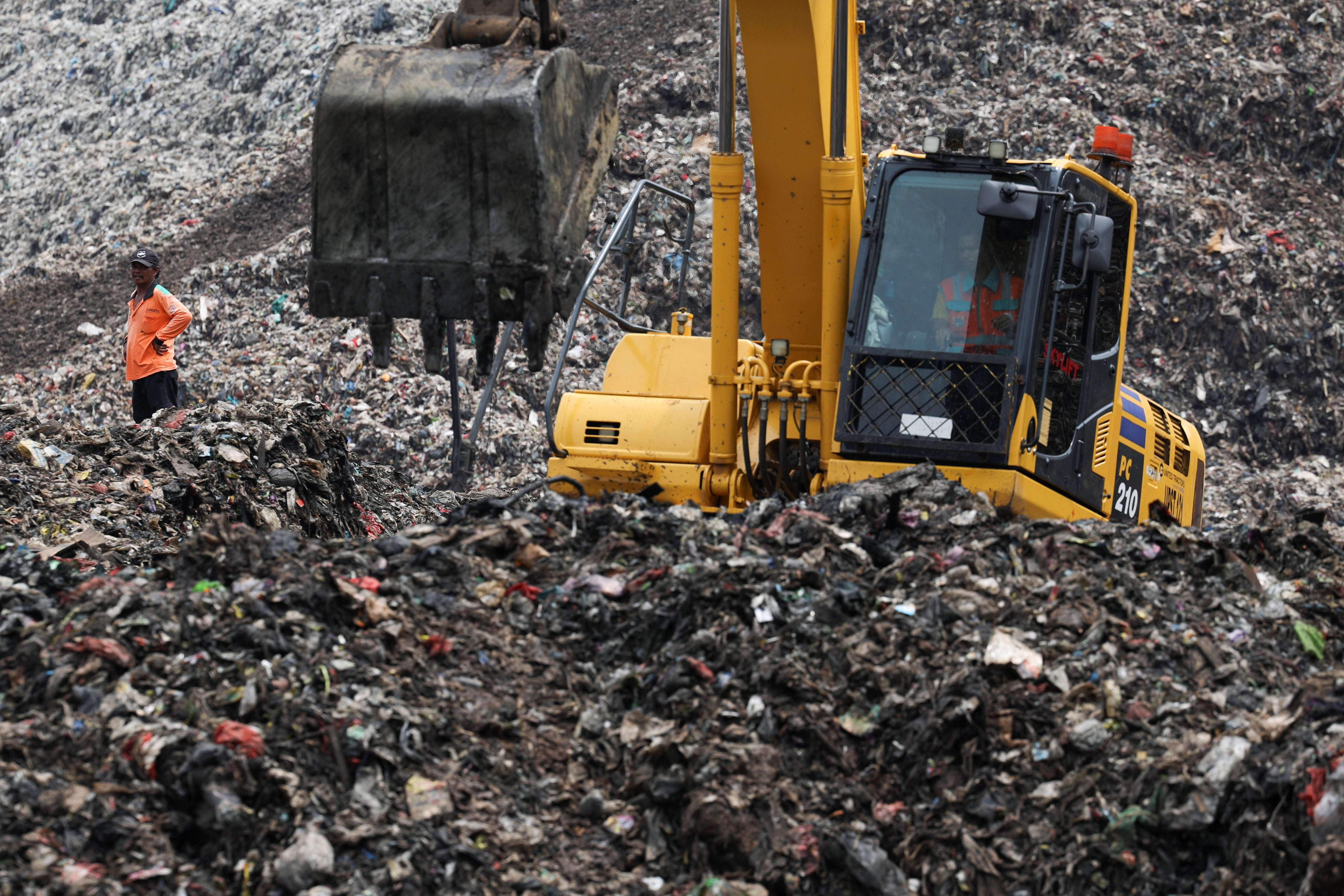 A worker stands amid garbage at the site of a collapse at the Bantar Gebang landfill, while an excavator operates during a rescue operation in Bekasi