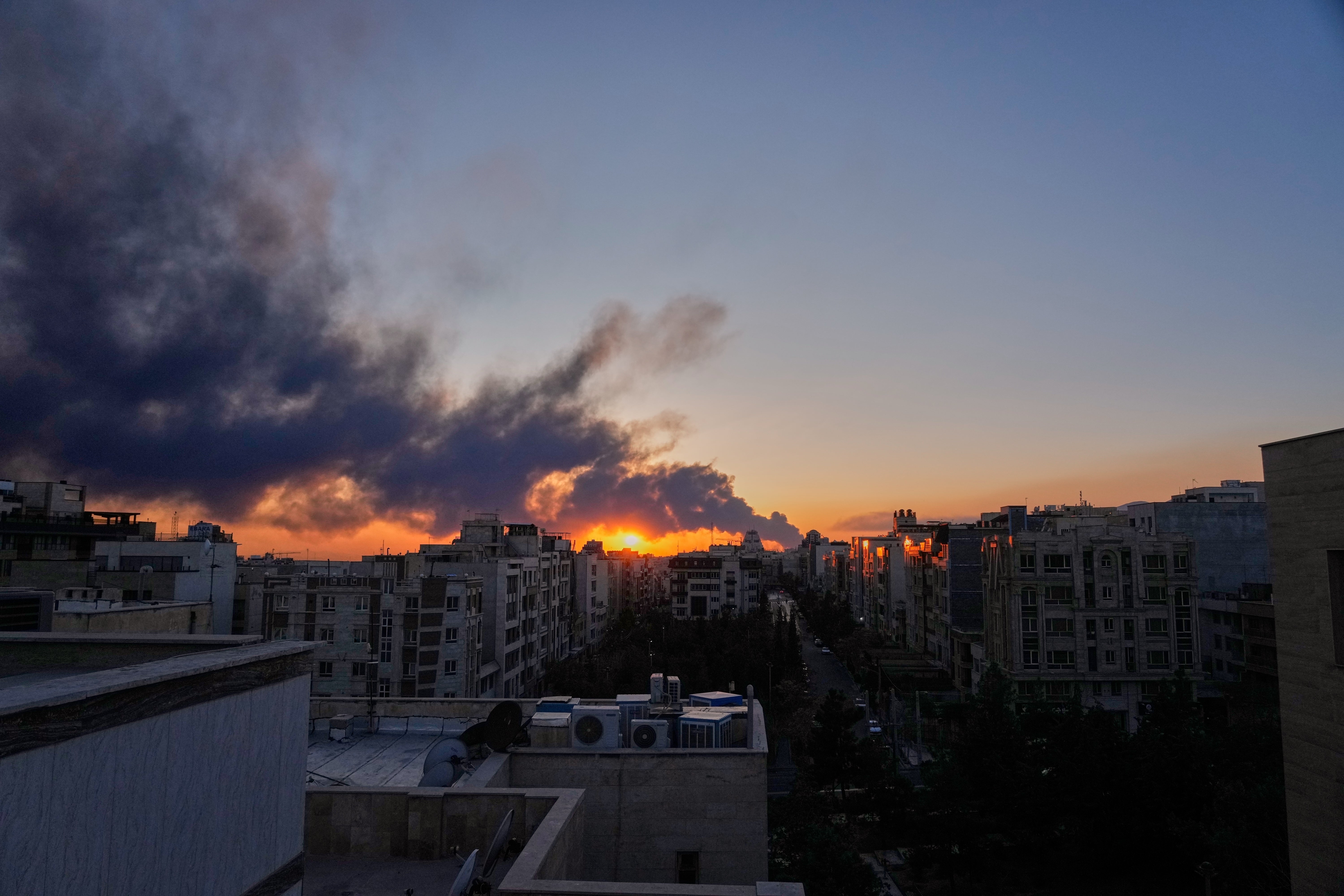 The sun sets behind a plume of smoke rising from a strike on Tehran