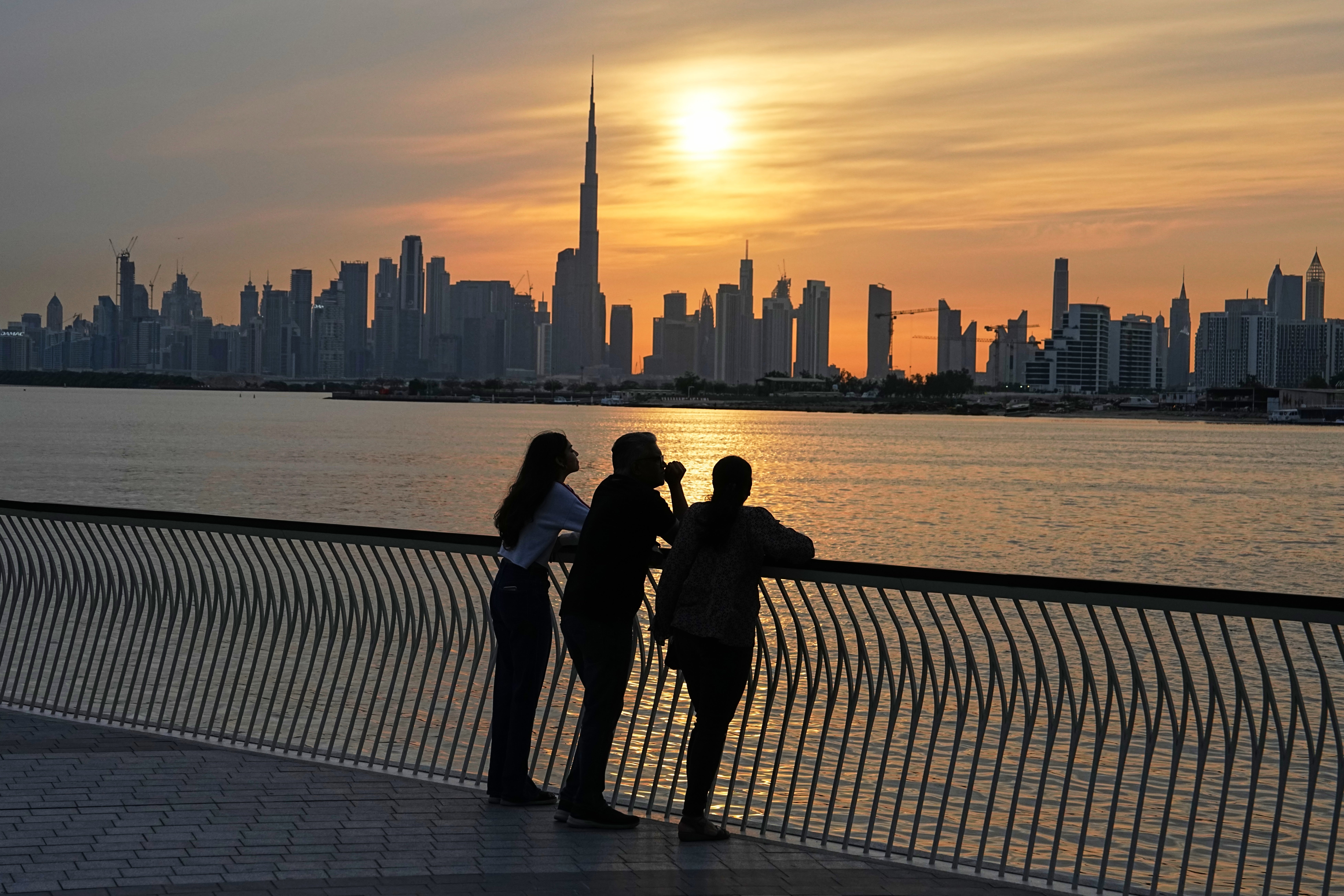 A family enjoys the sunset with the view of the city skyline and Burj Khalifa, at Dubai Creek Harbour in Dubai