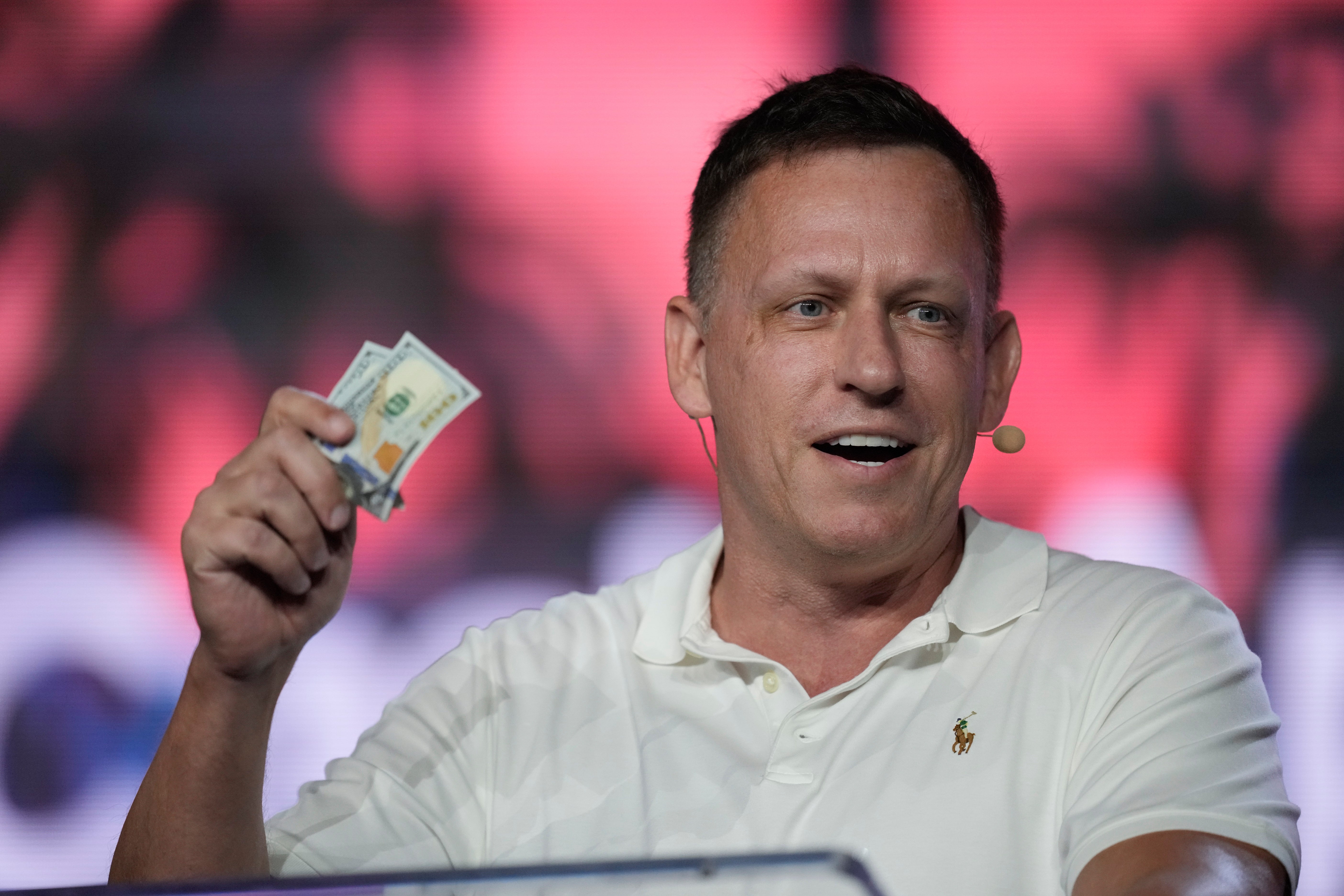 Peter Thiel, co-founder of PayPal and Palantir, offers a pair of hundred dollar bills to attendees during a keynote address at the Bitcoin Conference, April 7, 2022, in Miami Beach, Fla. (AP Photo/Rebecca Blackwell, File)