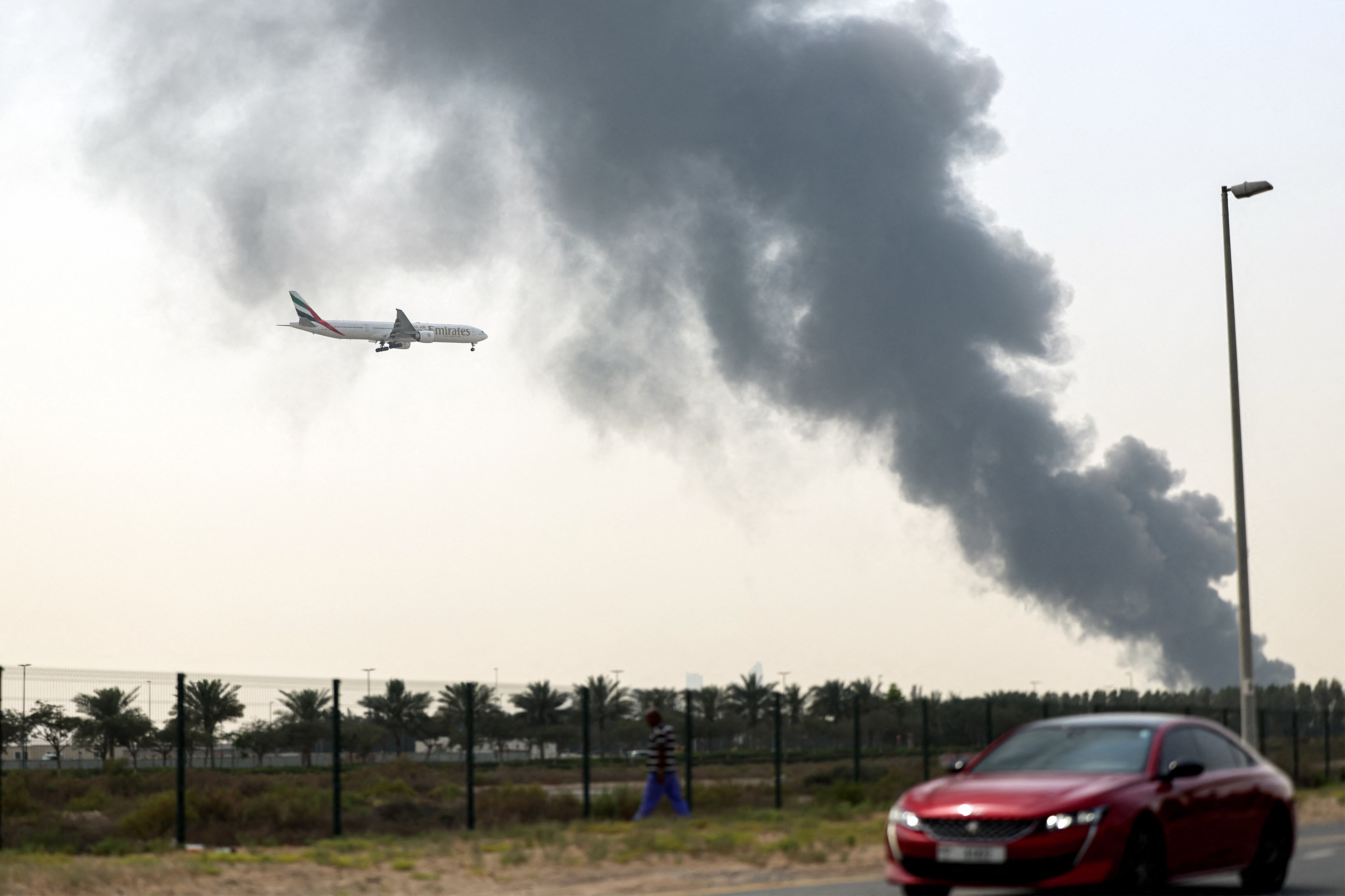 An Emirates Boeing 777 aircraft prepares for landing as a smoke plume rises from an ongoing fire near Dubai International Airport in Dubai on March 16