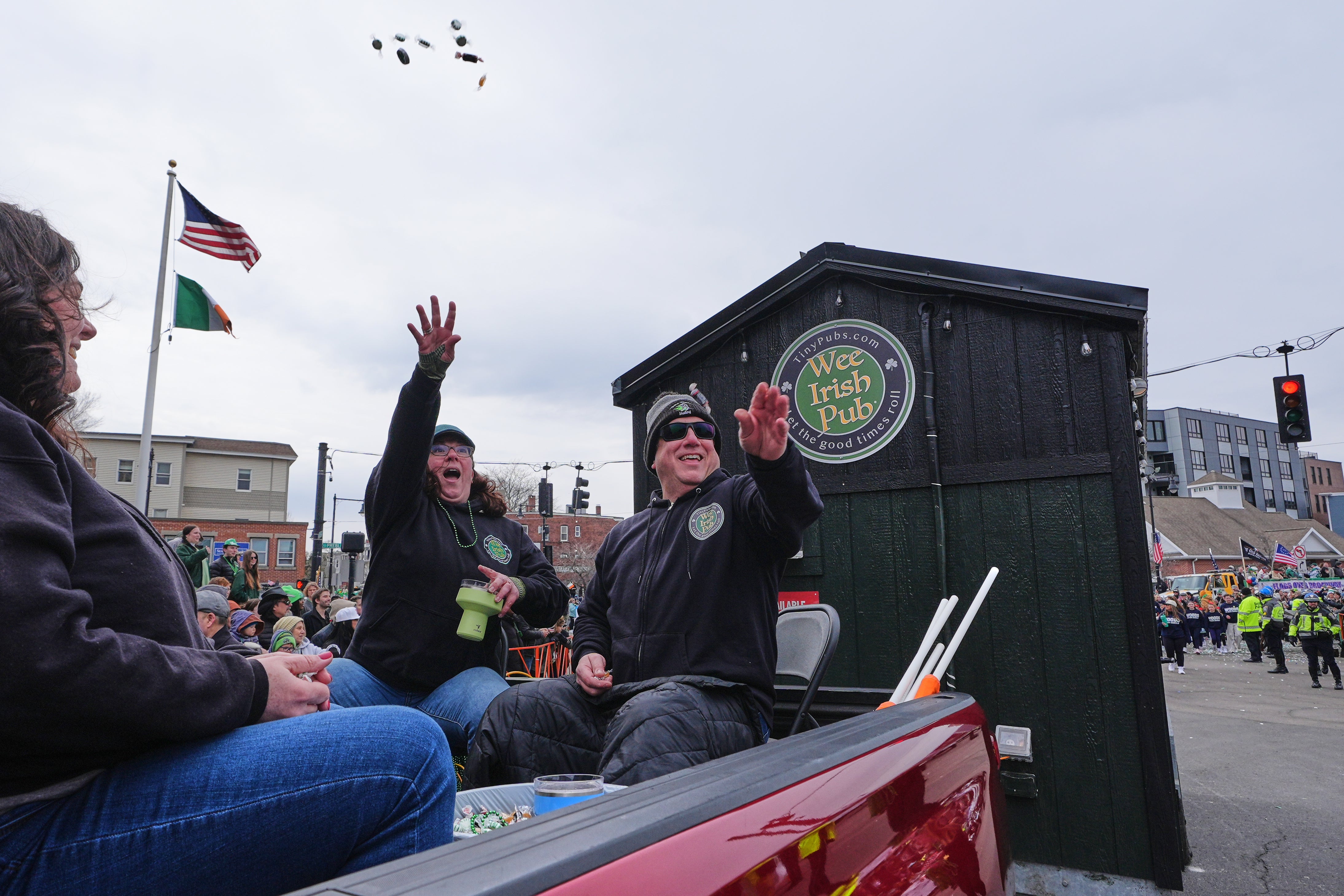 Dena Taylor and Tony DiDonato, right, toss candy to spectators while riding in a truck hauling the "Wee Irish Pub", a fully functioning mobile Irish pub built by two Massachusetts' brothers, during the annual St. Patrick's Day parade through the South Boston neighborhood, Sunday, March 15, 2026. (AP Photo/Charles Krupa)