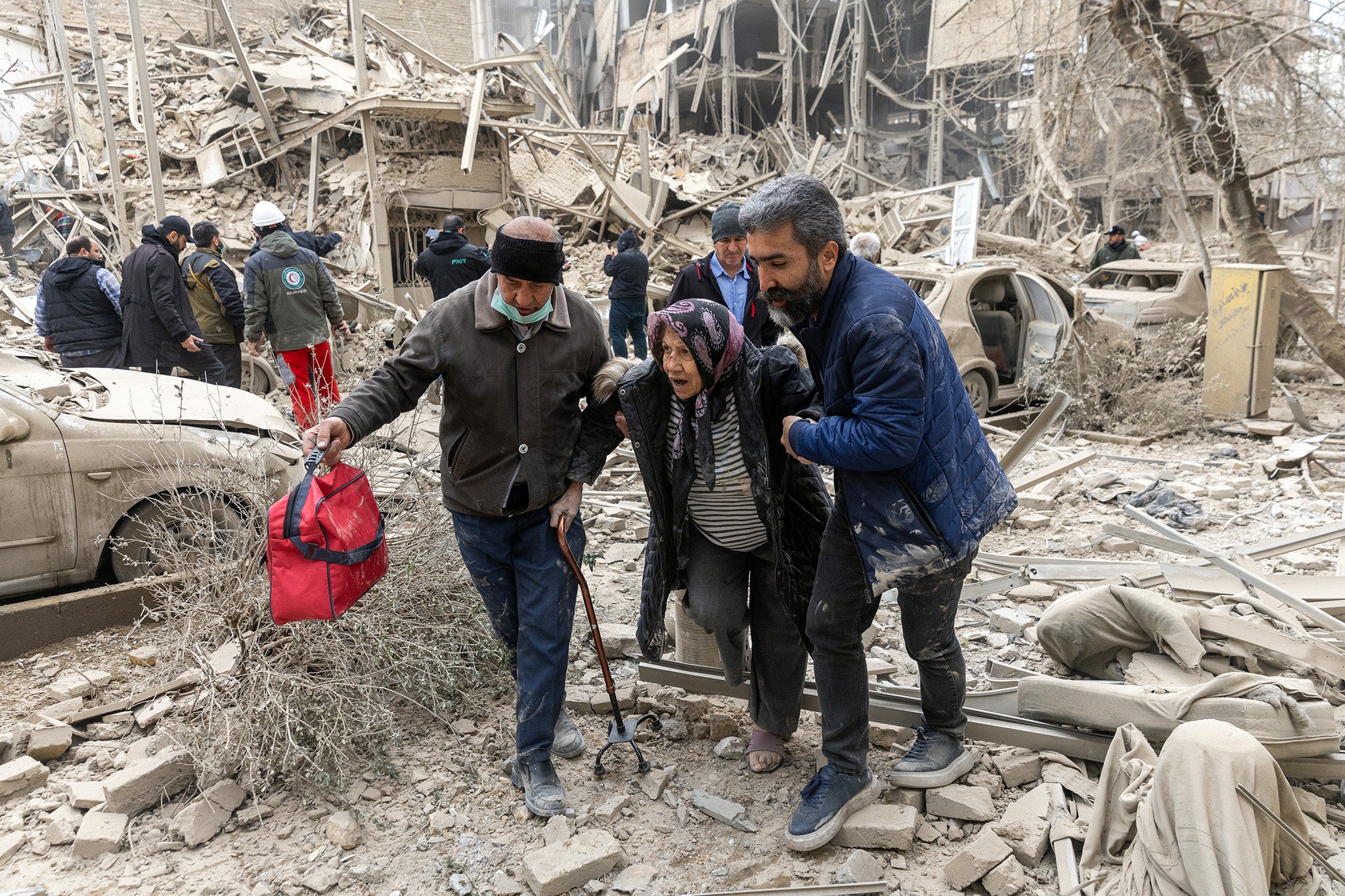 An elderly woman is helped from the scene of a strike on a residential building on March 16, 2026 in central Tehran, Iran
