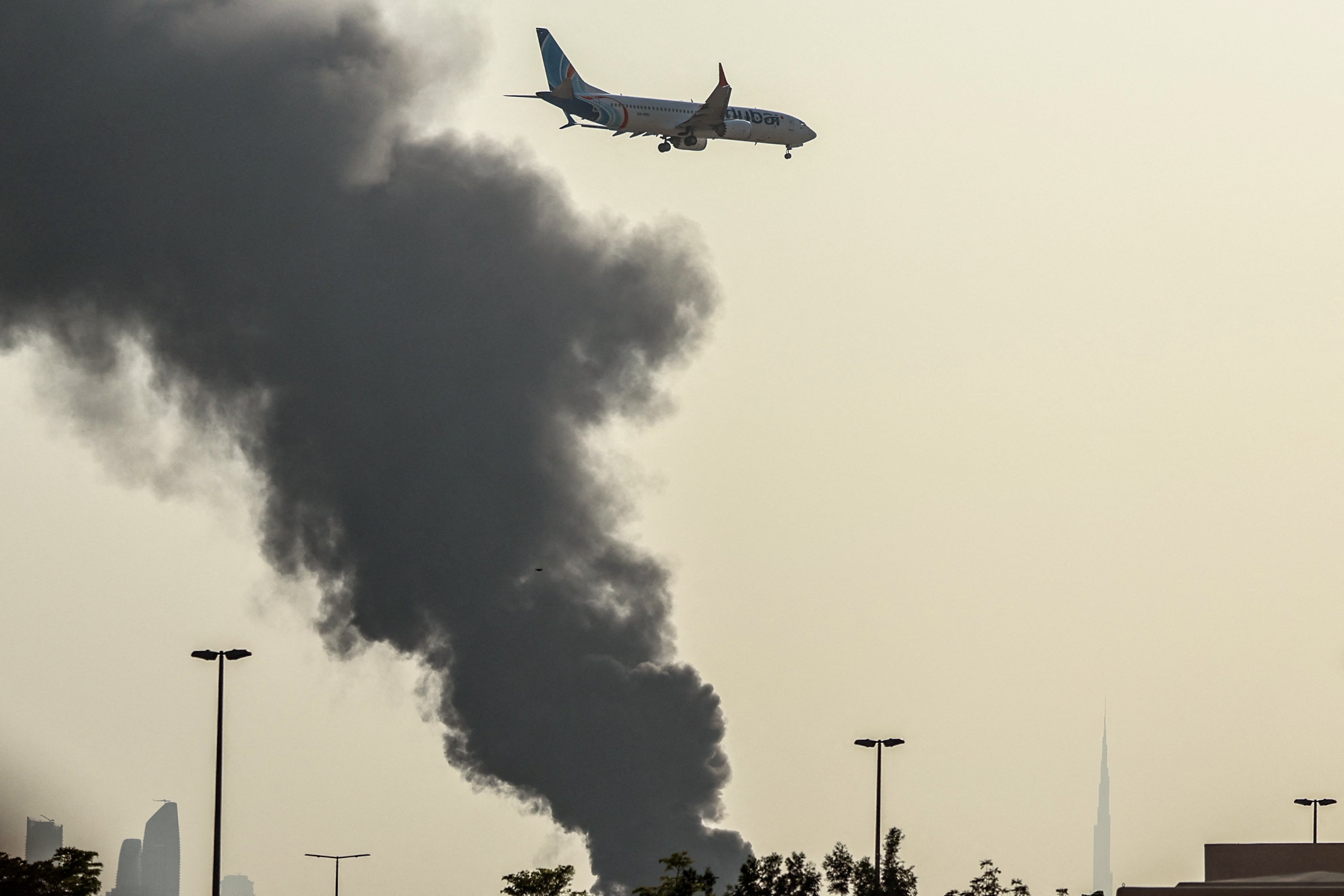 An international low coast FlyDubai aircraft prepares for landing as a smoke plume rises from an ongoing fire near Dubai International Airport in Dubai on March 16, 2026