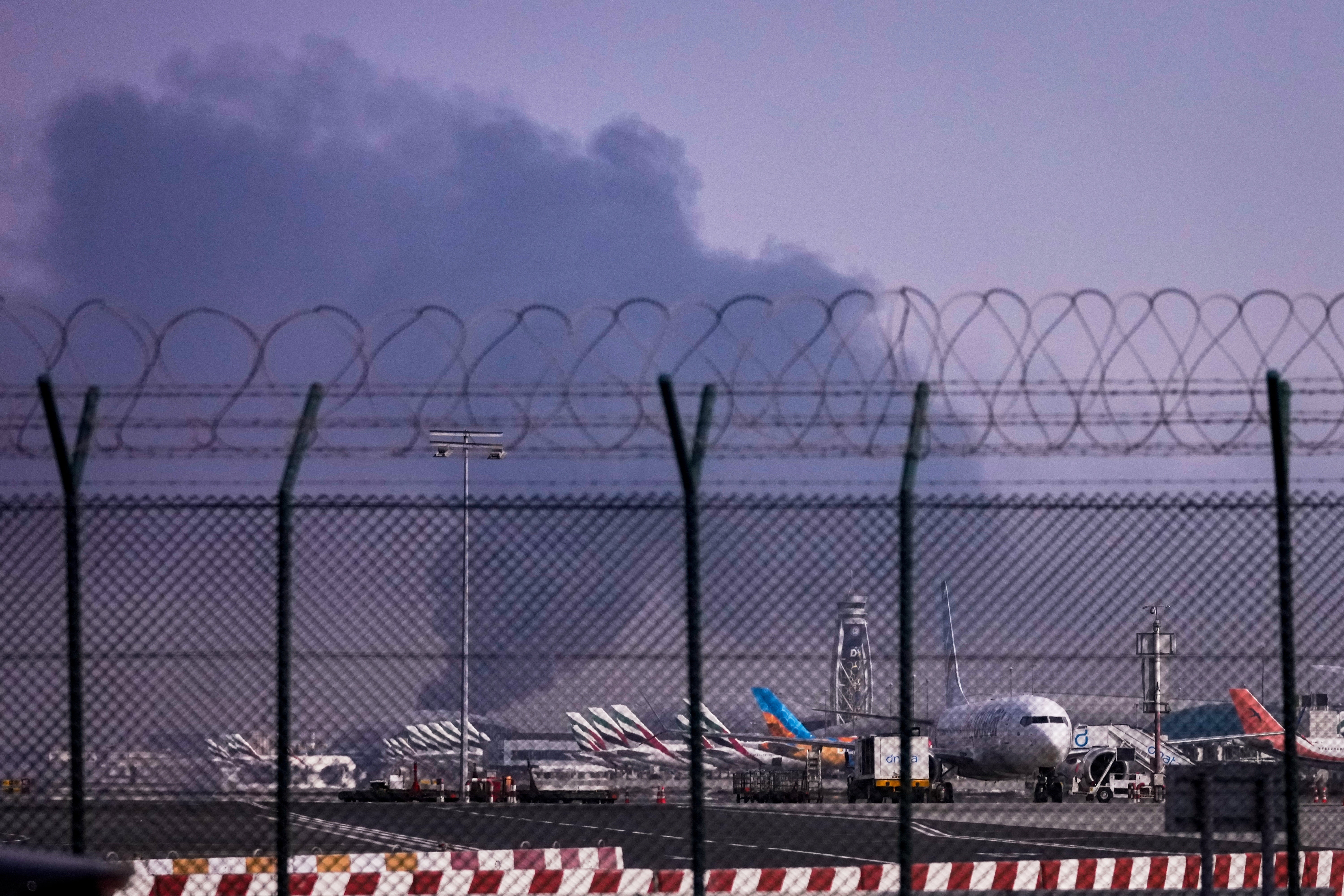 Planes are parked at Dubai International Airport as smoke rises following a drone strike on 16 March