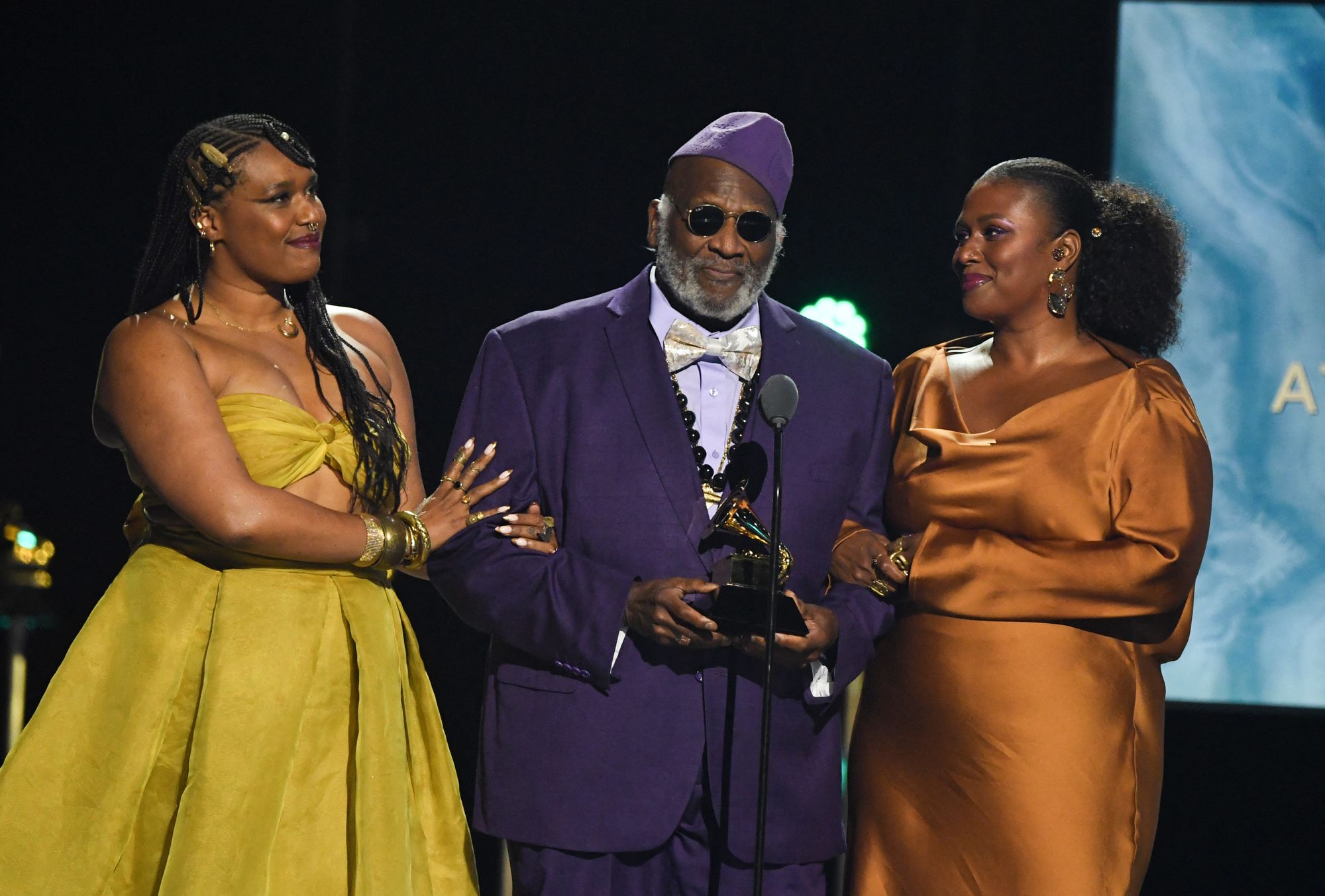 Taj Mahal accepting the Grammy for Best Traditional Blues Album for ‘Swingin’ Live at The Church in Tulsa’ in 2025, flanked by his daughters Zoe Moon and Deva Mahal