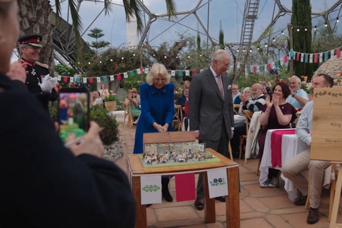 King and Queen laugh as they struggle to cut cake with sword