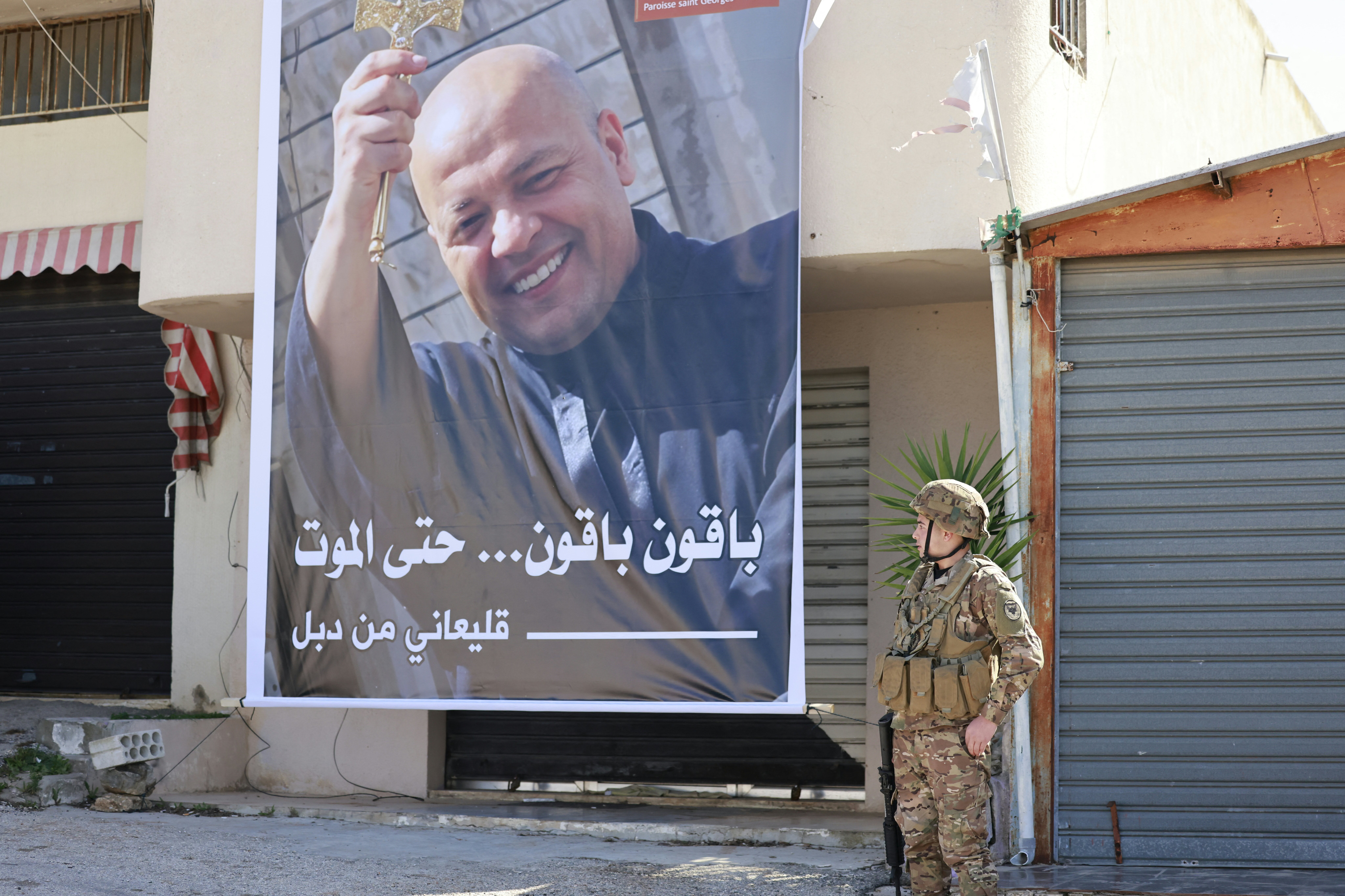 A Lebanese army soldier stands next to a poster of the village's priest, Father Pierre al-Rahi during his funeral
