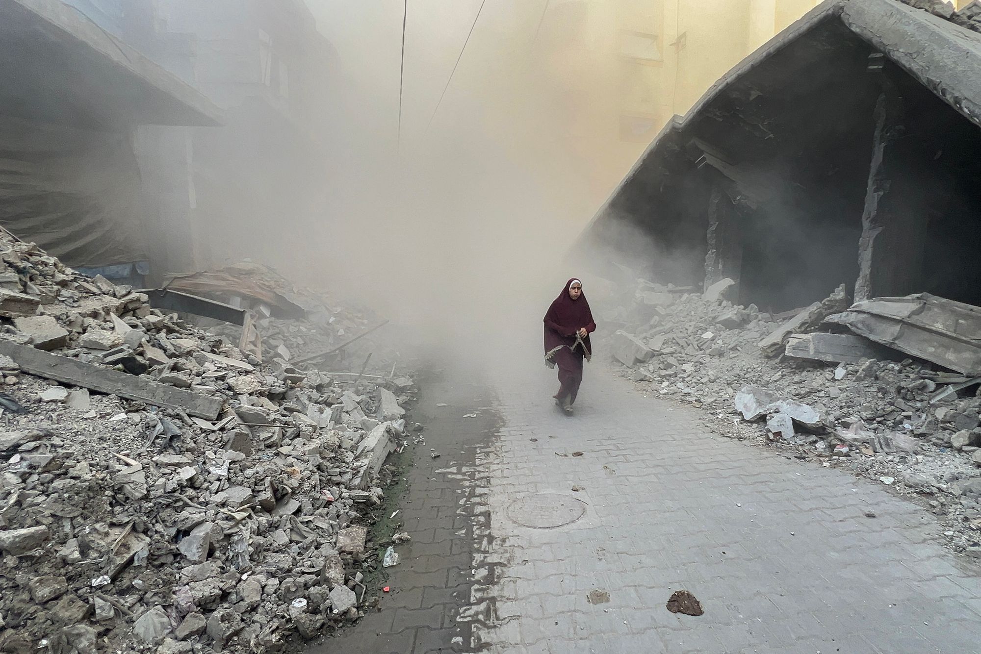 A Palestinian young woman rushes away from the site of Israeli air strikes on a six-storey building in the Saftawi neighborhood west of Jabalia in the northern Gaza Strip on August 19, 2025