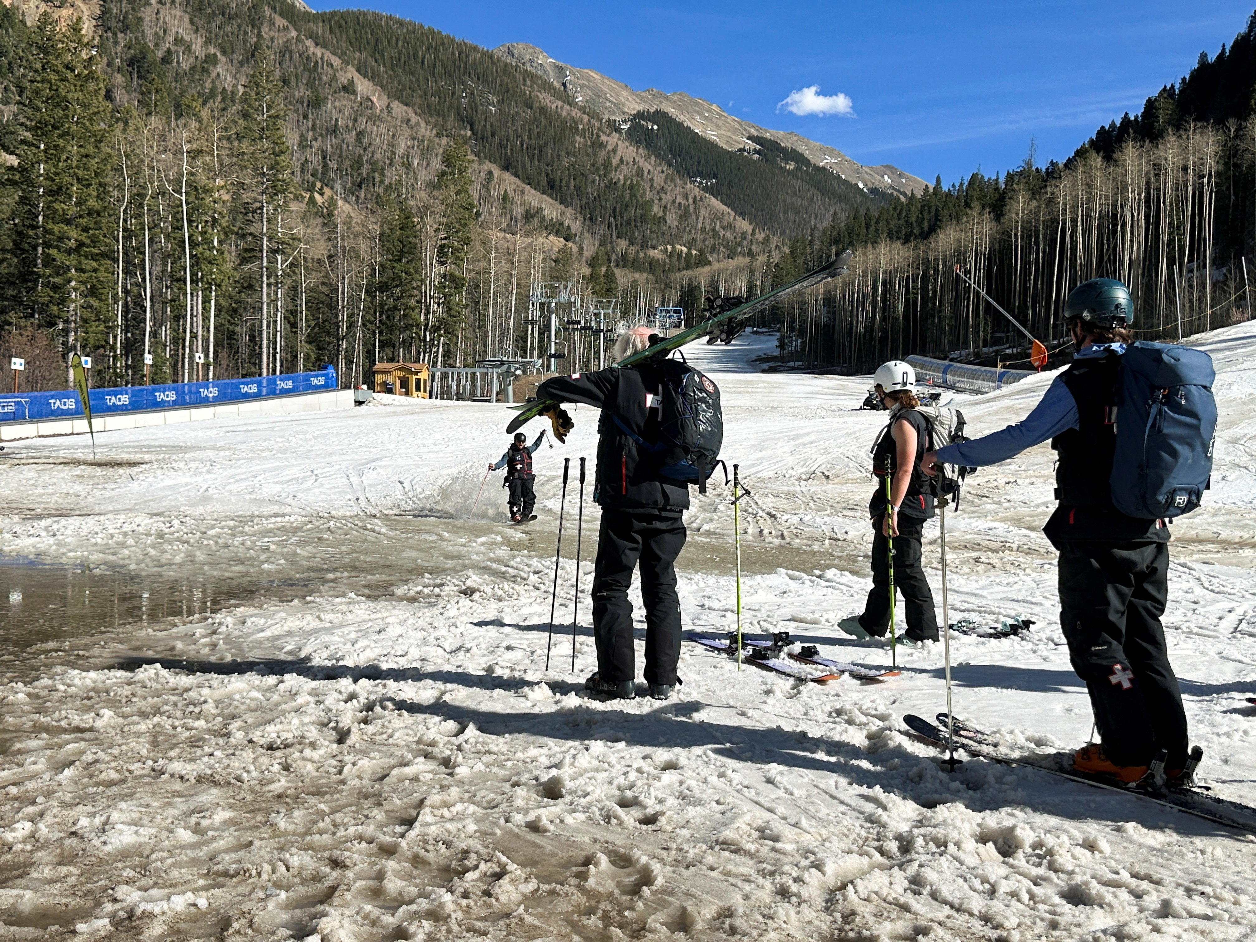 A skier "water skis" over a puddle as others look on at Taos Ski Valley