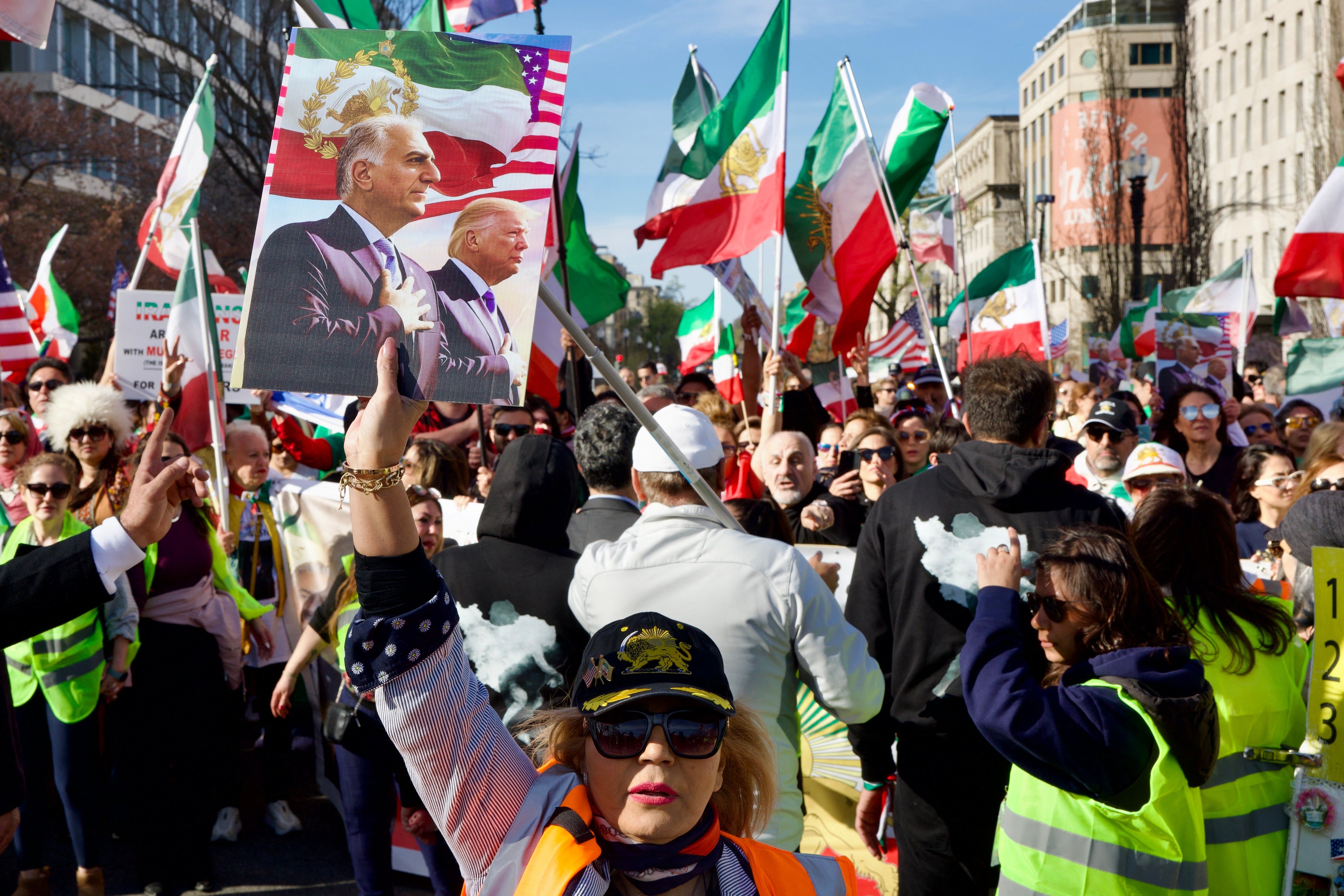 A woman holds up a sign featuring an image of Reza Pahlavi, son of the last shah of Iran, and US President Donald Trump as demonstrators march toward the White House during a rally in support of Iranians' fight for freedom, in Washington, DC, on March 29, 2026. The event, organized by DCProtests4Iran, brought together members of the Iranian diaspora from the Washington, DC metropolitan area and surrounding states. (Photo by Amid FARAHI / AFP via Getty Images)