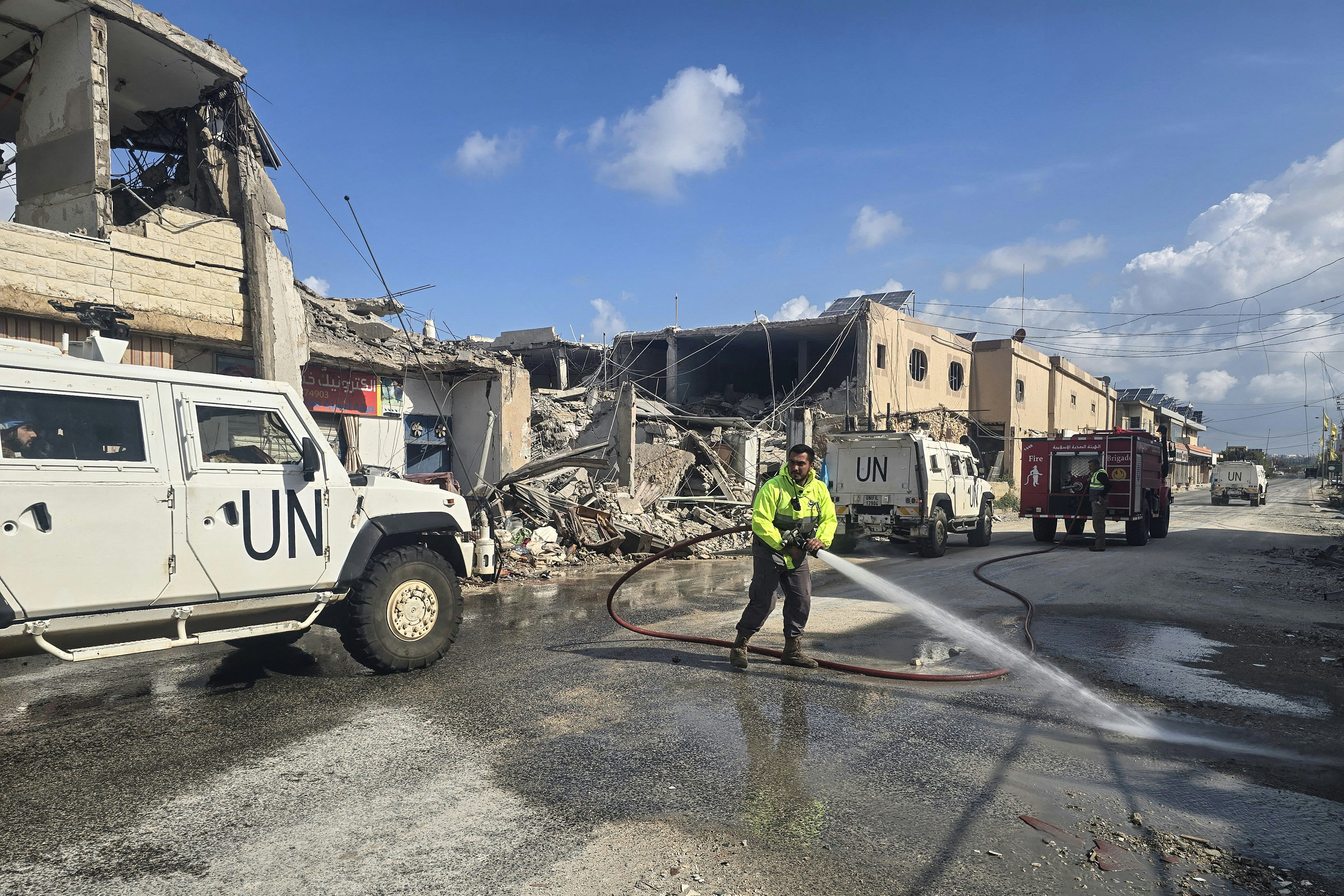 United Nations peacekeepers with the UN Interim Force in Lebanon (UNIFIL) drive past firefighters clearing the road at the site of an overninght Israeli airstrike in the area of Naqura in southern Lebanon