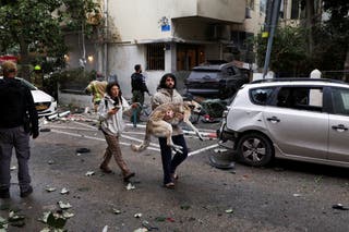 A man carries a dog to a shelter as sirens sound in Tel Aviv