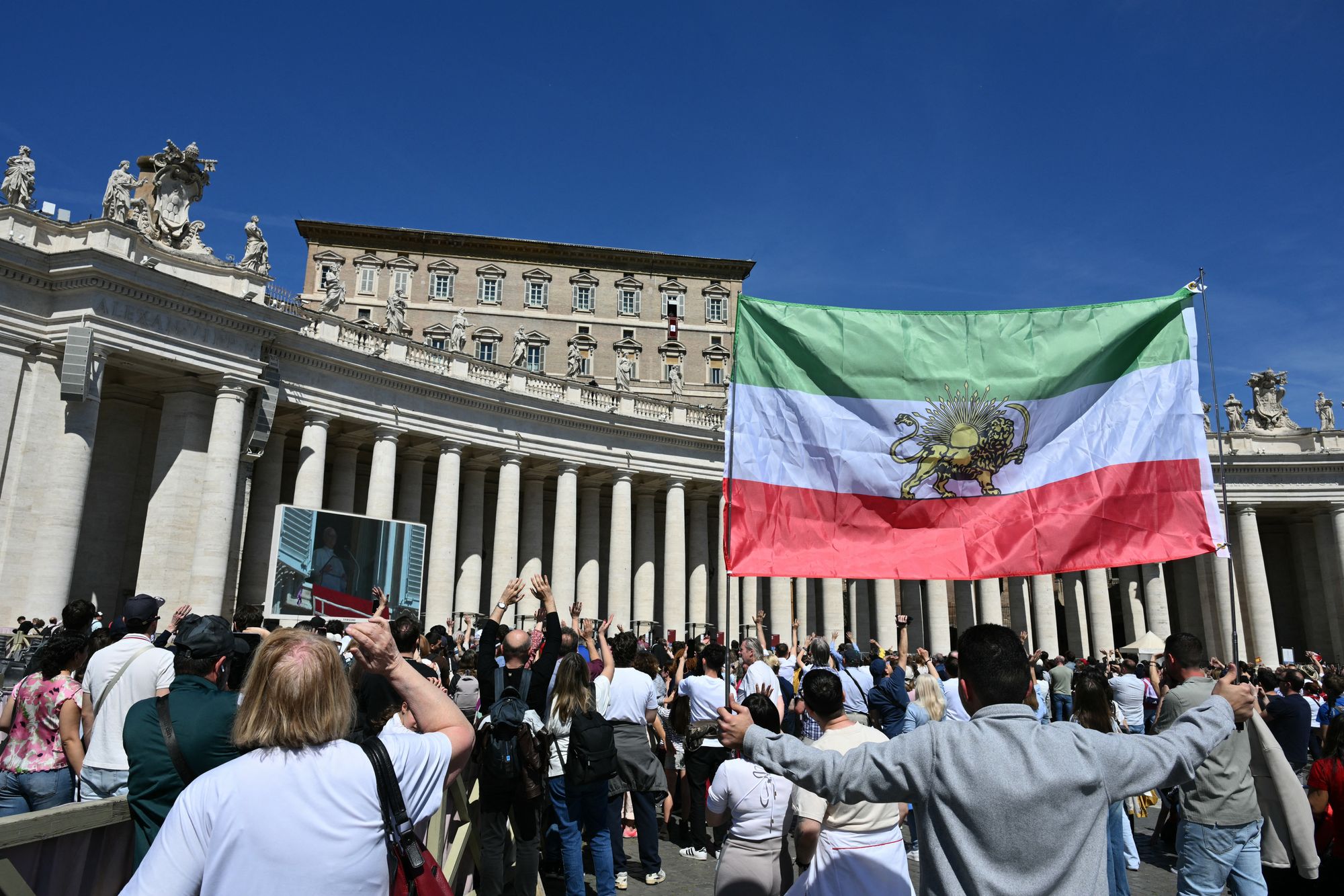 A man holds the Iranian prerevolution lion and sun flag as Pope Leo XIV addresses the crowd from the window of the apostolic palace overlooking St. Peter's square on April 6, 2026