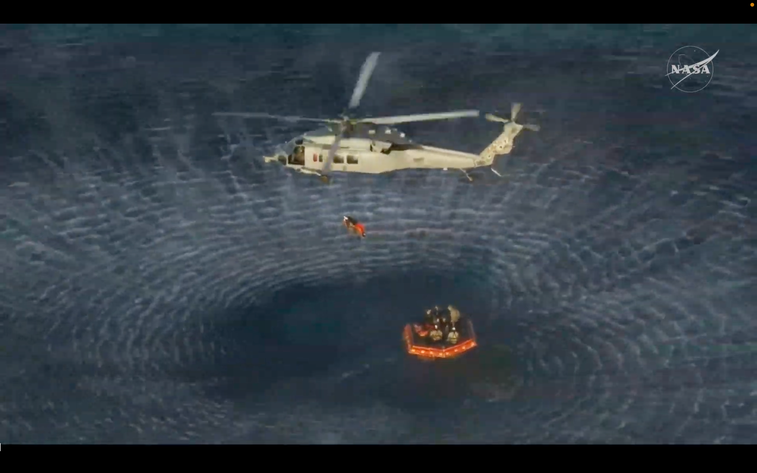 One of the Artemis II astronauts is hoisted beneath a helicopter to a U.S. Navy recovery ship