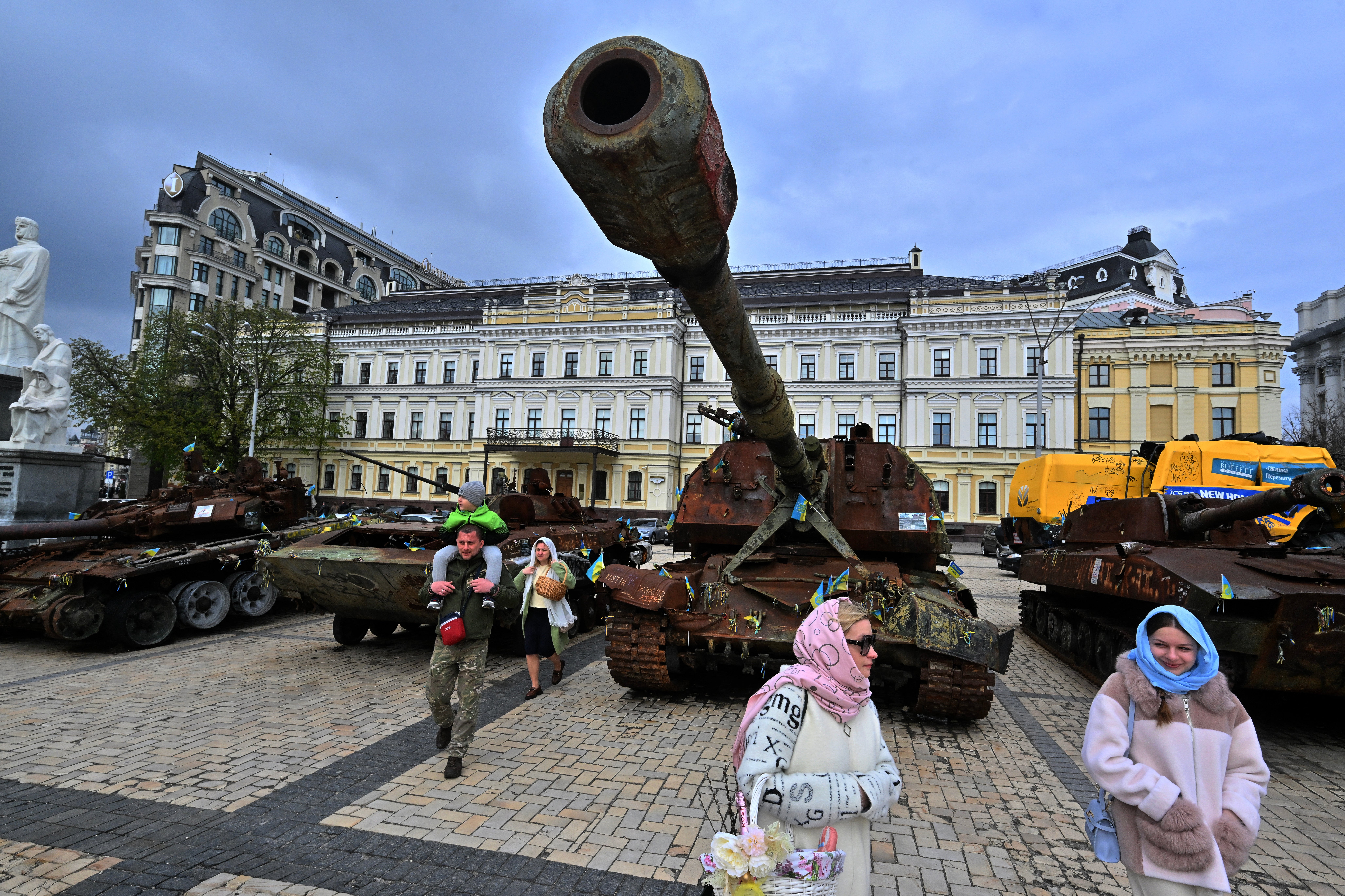 Местные жители несут корзины с традиционными куличами и яйцами, проходя мимо выставки уничтоженной российской военной техники под открытым небом во время празднования Пасхи в Киеве.
