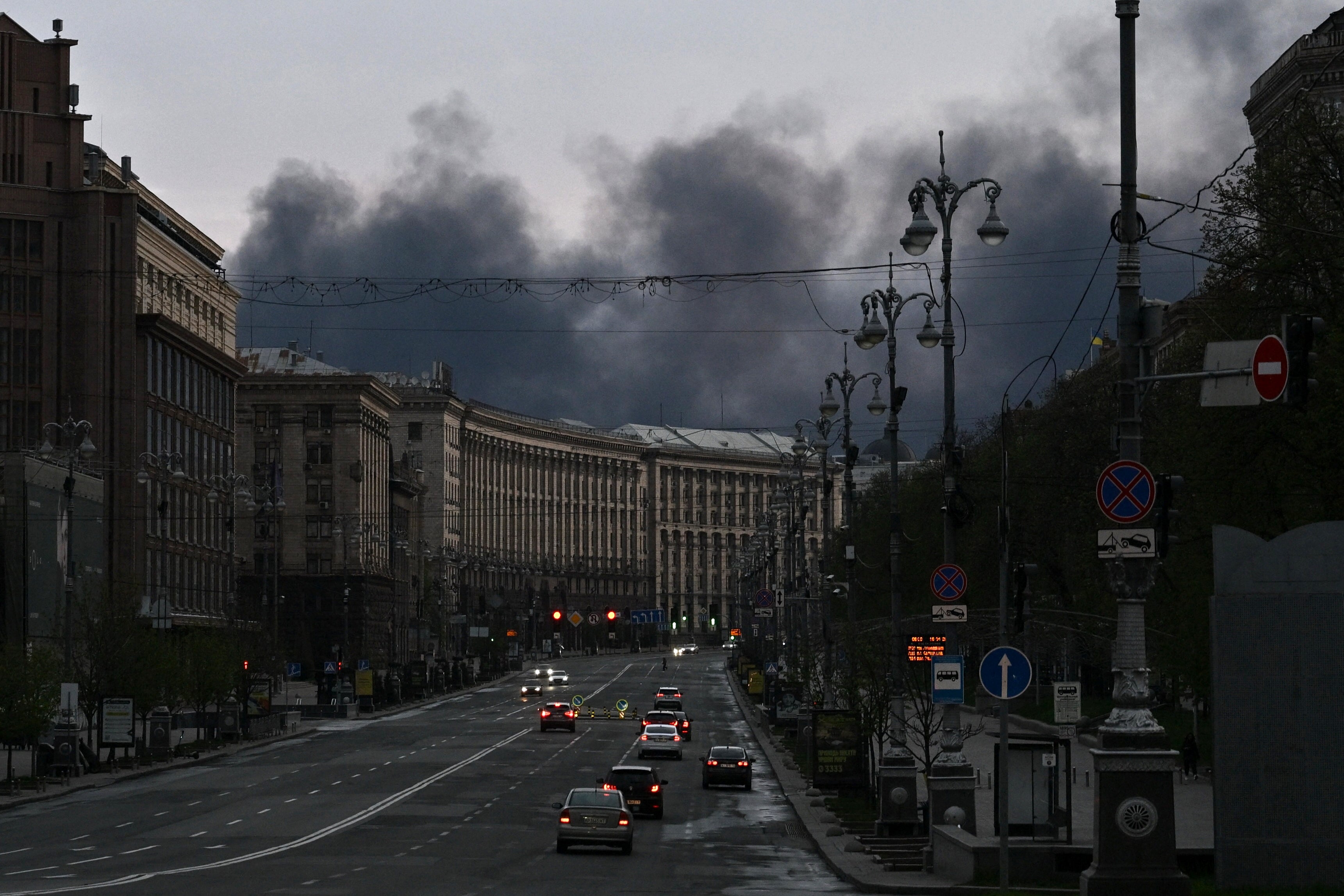 Cars drive along Khreshchatyk Street as smoke rises above buildings in the background following an air attack in Kyiv