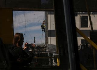 A woman rides a bus and takes pictures as a worker installs an OSB board in place of a broken window of a hotel hit by a yesterday's Russian missile and drone strike, amid Russia's attack on Ukraine, in Kyiv, Ukraine April 17,