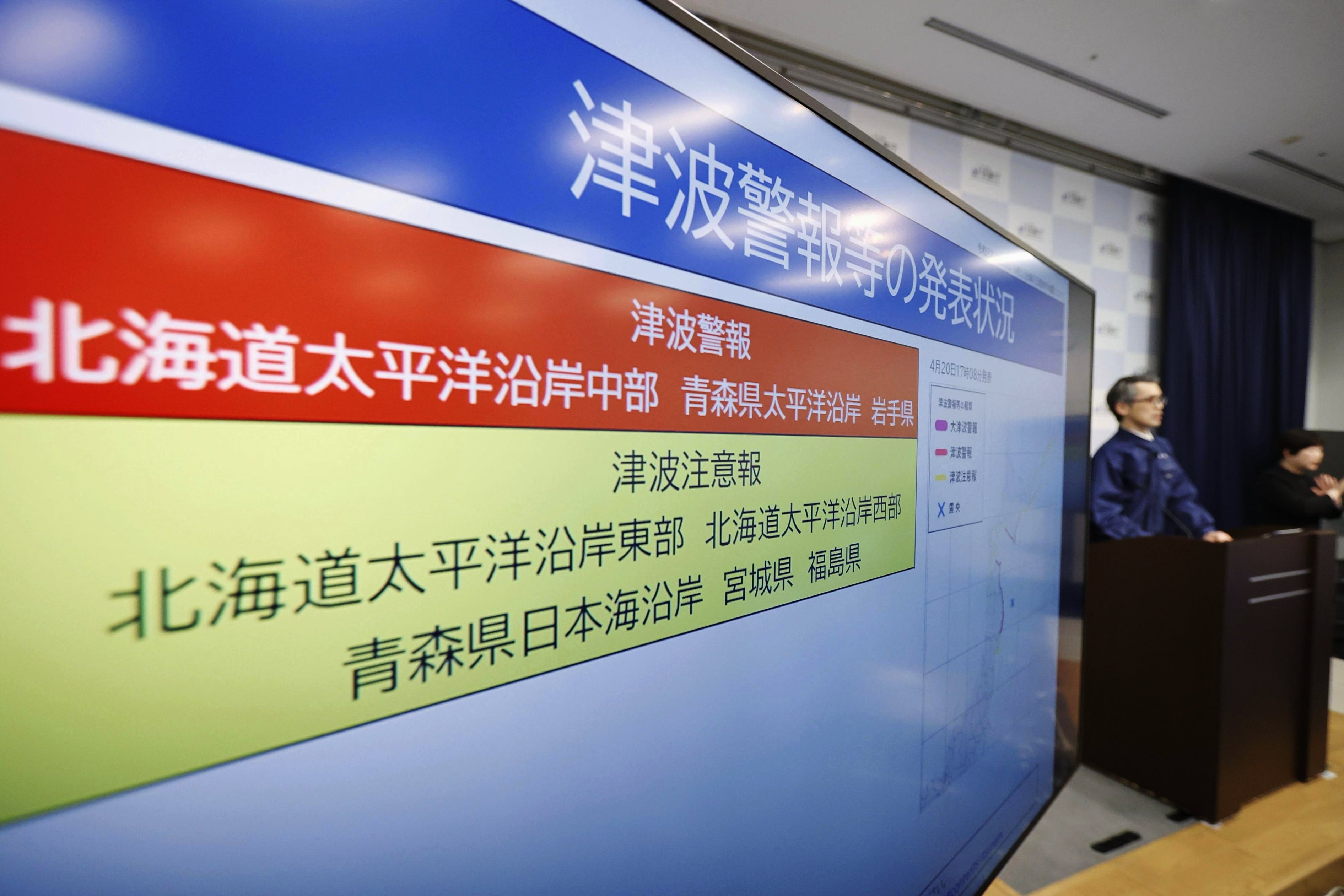 An official of the Japan Meteorological Agency speaks near a monitor showing a tsunami alert during a news conference at the agency in Tokyo