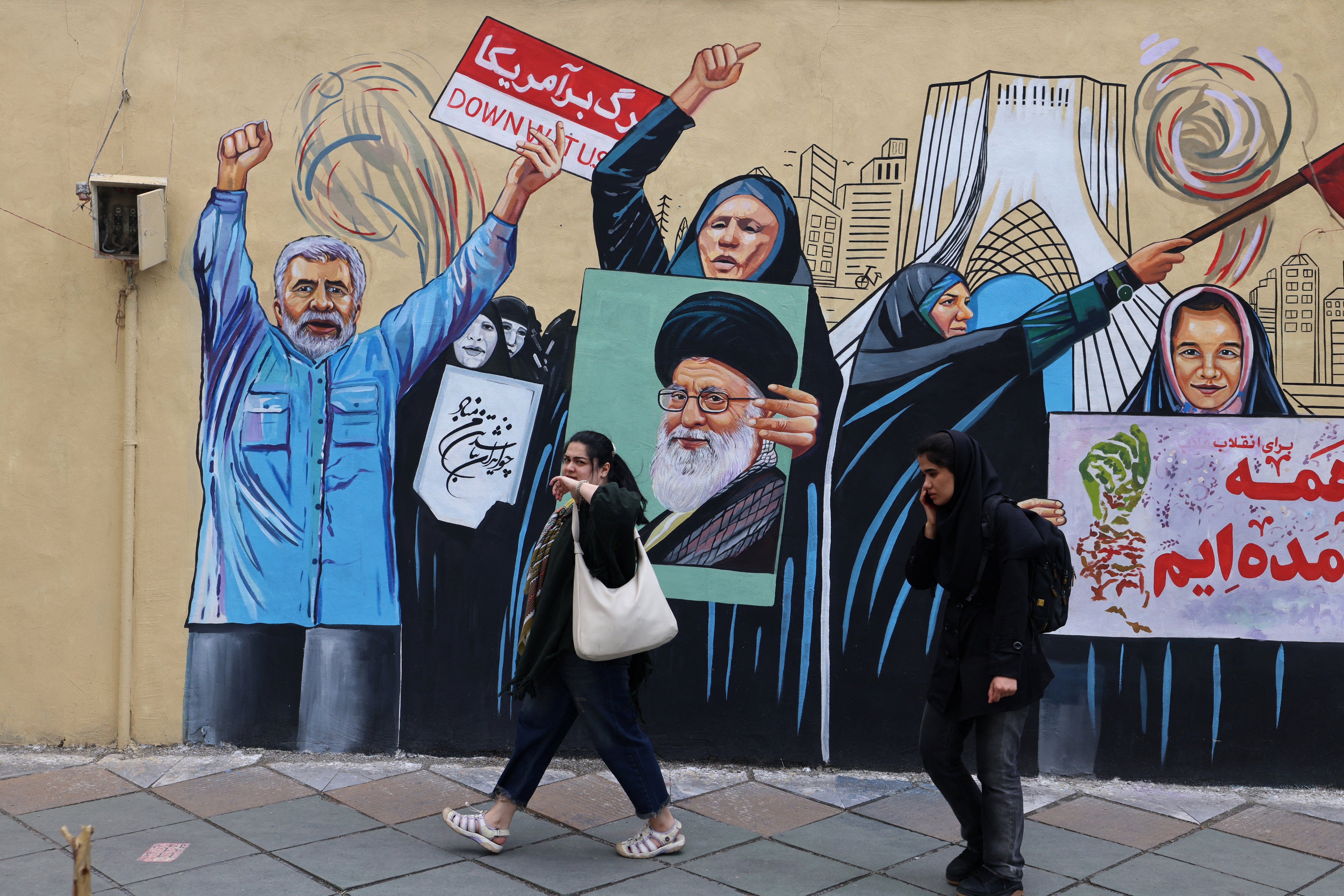 People walk past an anti-USA and anti-Israel mural depicting the late Iranian supreme leader Ayatollah Ali Khamenei, in Tehran on 21 April
