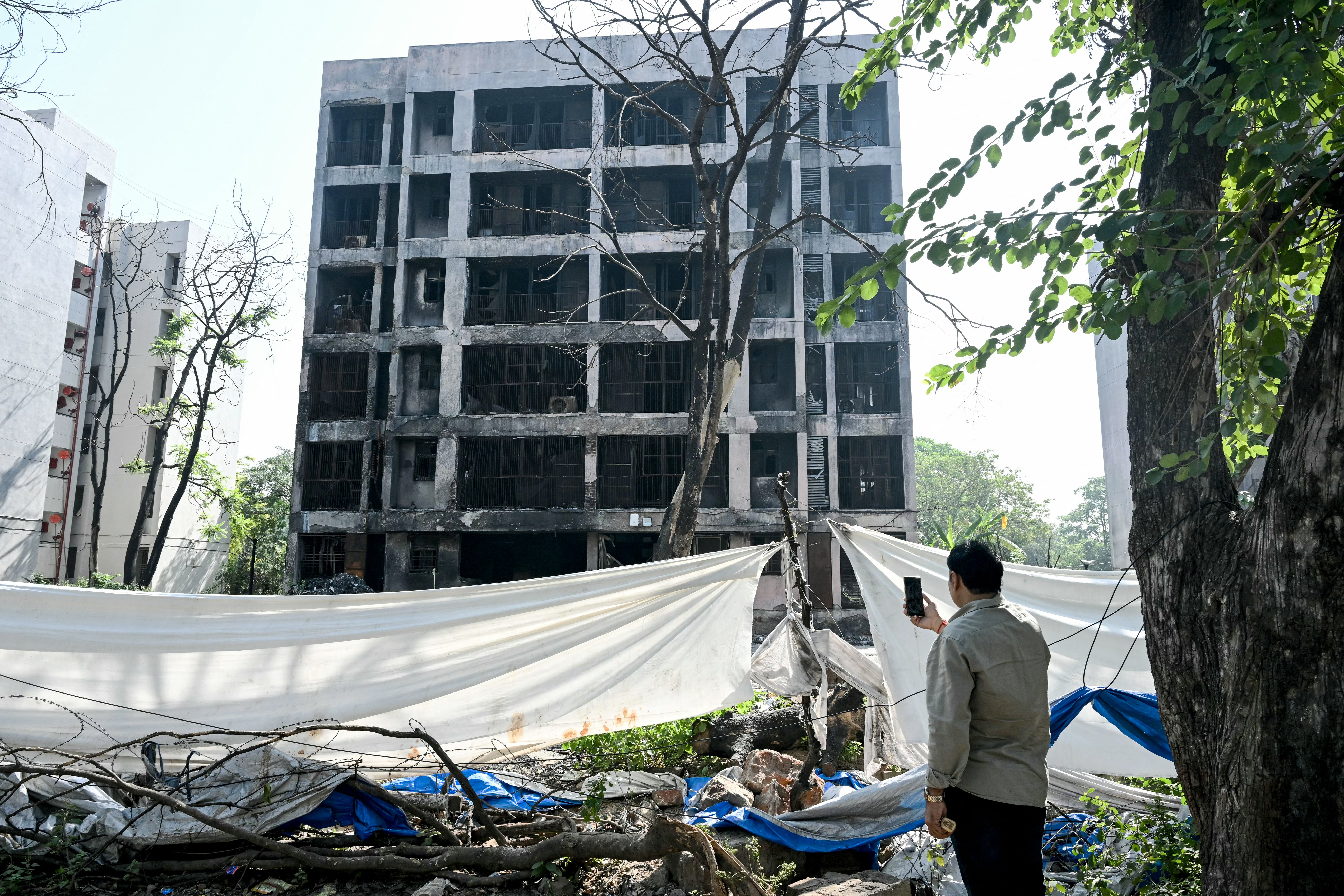 A man takes visuals of a charred building at the accident site of Air India flight AI171 that crashed into a residential area near the airport on June 12 in Ahmedabad