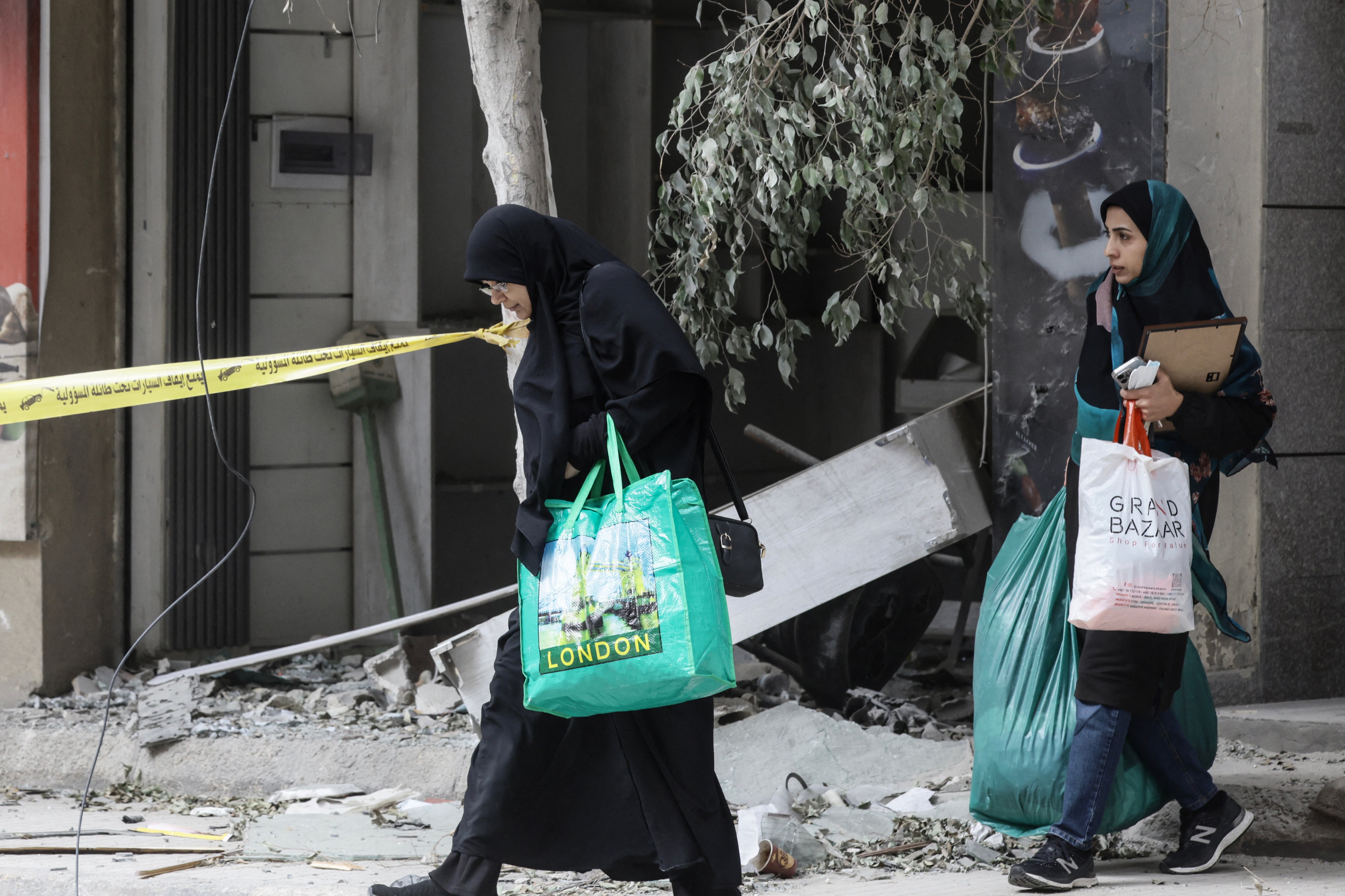 Women carrying belongings walk past the debris of a destroyed building in the Haret Hreik area of Beirut's southern suburbs on April 20, 2026