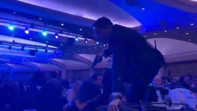 A screen grab taken from a video filmed by an AFP reporter shows an armed agent climbing over chairs as they move to the stage after loud bangs were heard during the White House Correspondents' dinner at the Washington Hilton in Washington, DC, on April 25, 2026.