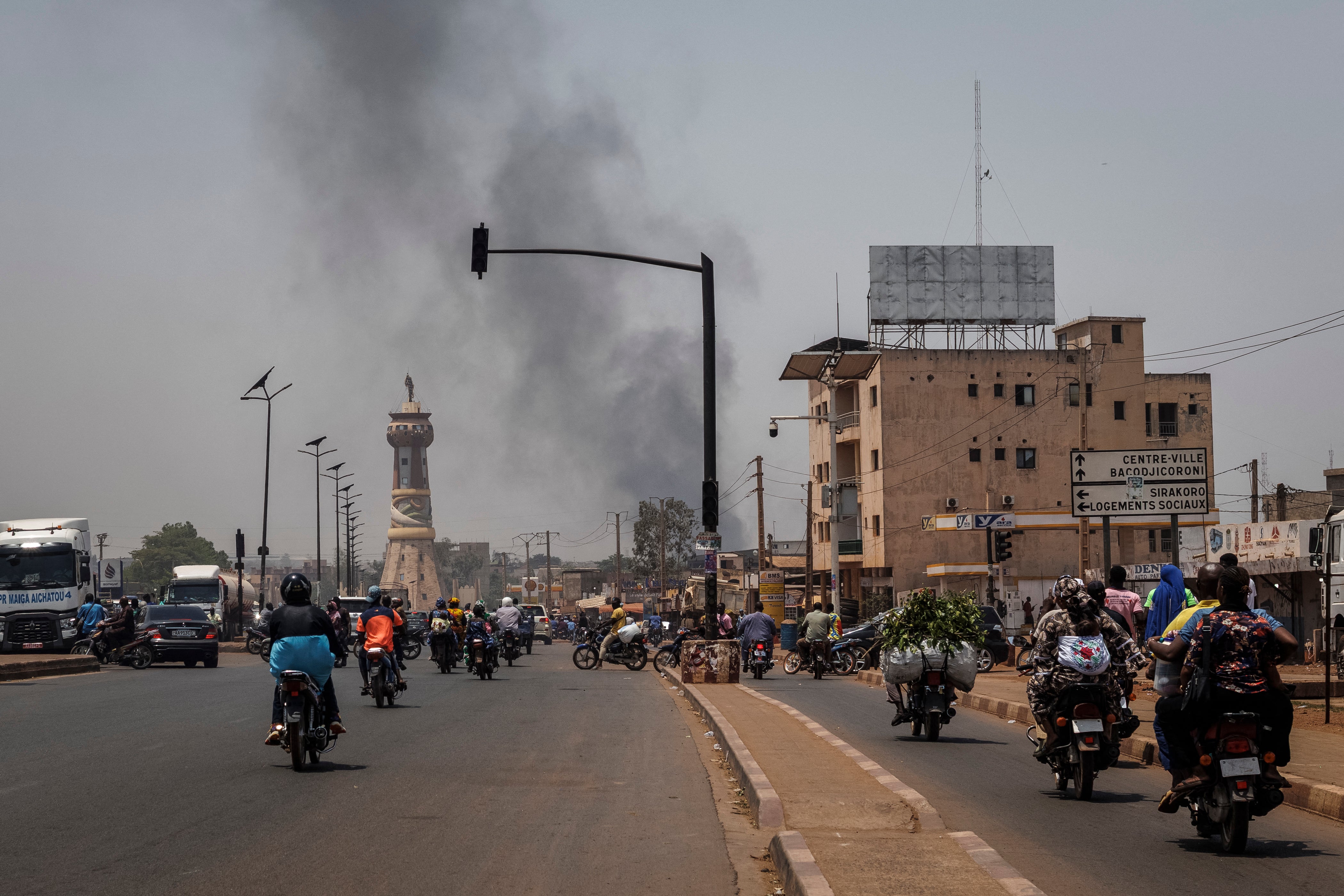 A column of black smoke rises above buildings as traffic passes the Africa Tower monument in Bamako on Sunday