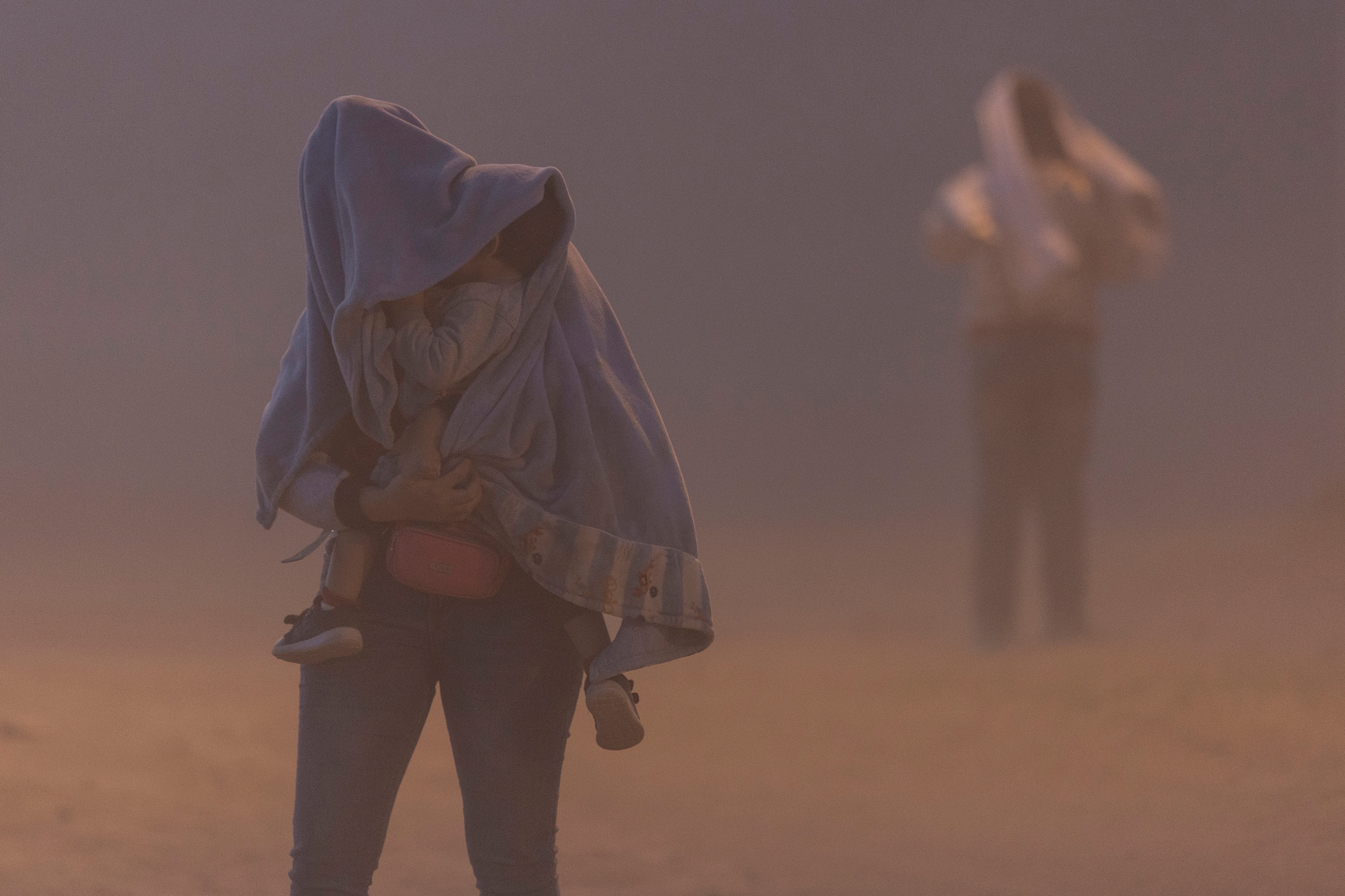 An immigrant mother and child from Venezuela walk through a dust storm while waiting to be processed for asylum claims in El Paso, Texas, in May 2023. Dust storms can cause reduced visibility