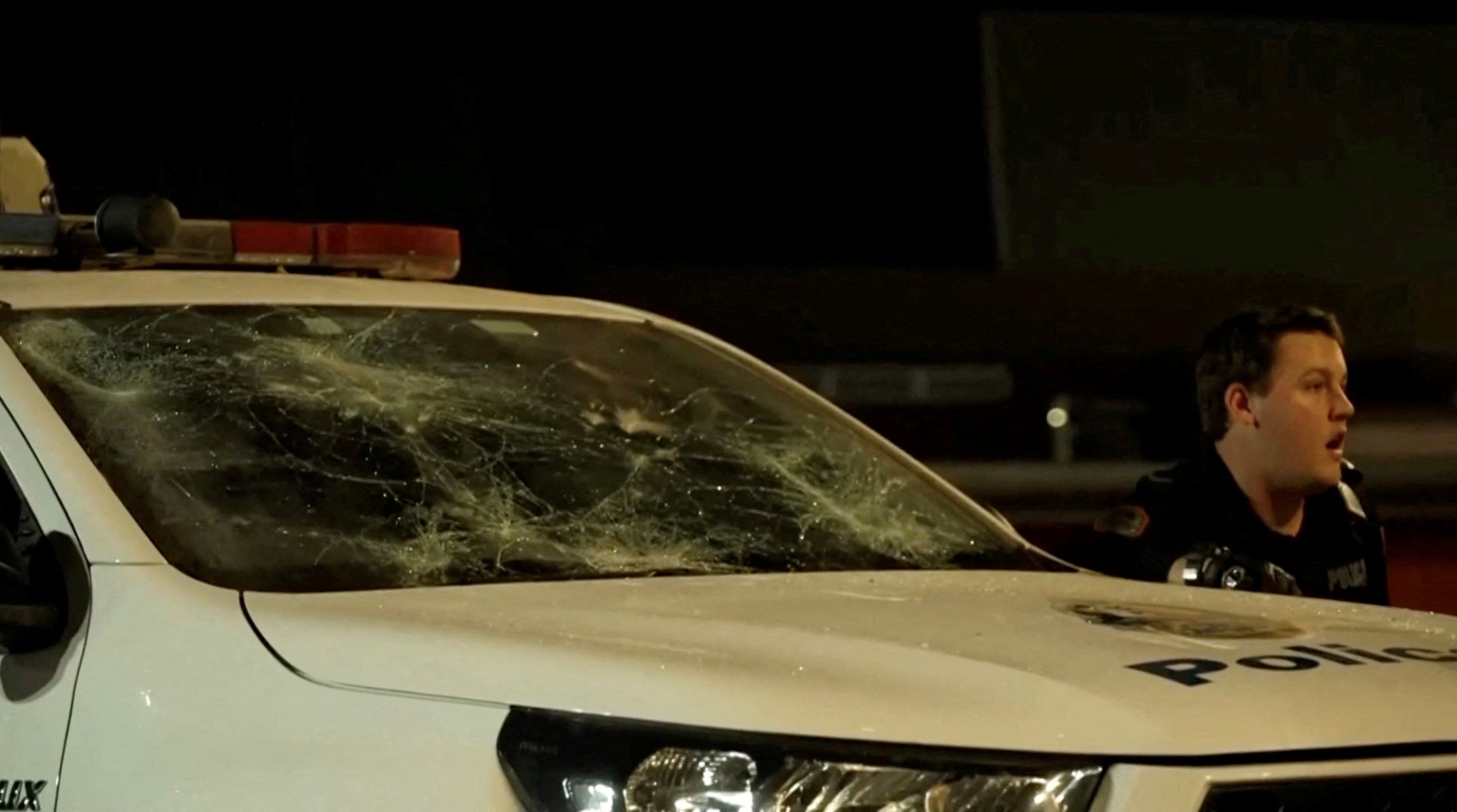 A police officer reacts next to a damaged vehicle during community unrest outside Alice Springs Hospital