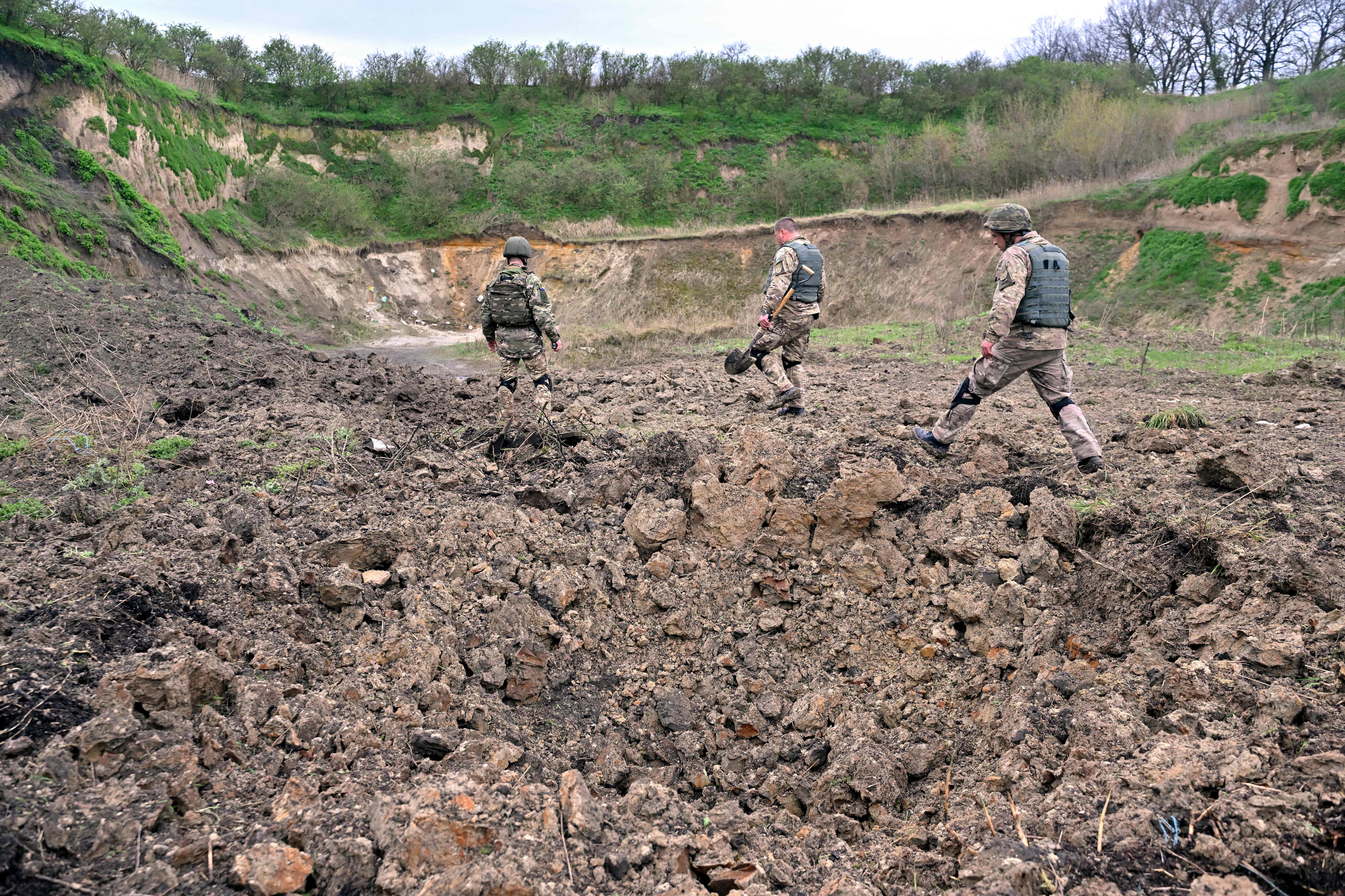 Deminers of Ukrainian Emergency Service walk past a crater following the explosion of anti-tank mines and other explosive materials, found in the town of Bucha