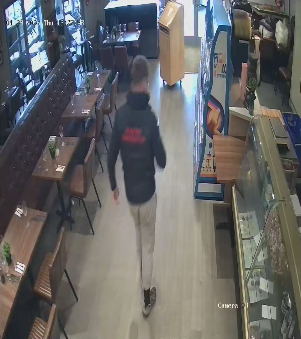 Suspect looks down at his mobile phone as he walks out of Relentless Steak and Lobster after allegedly not paying for their food