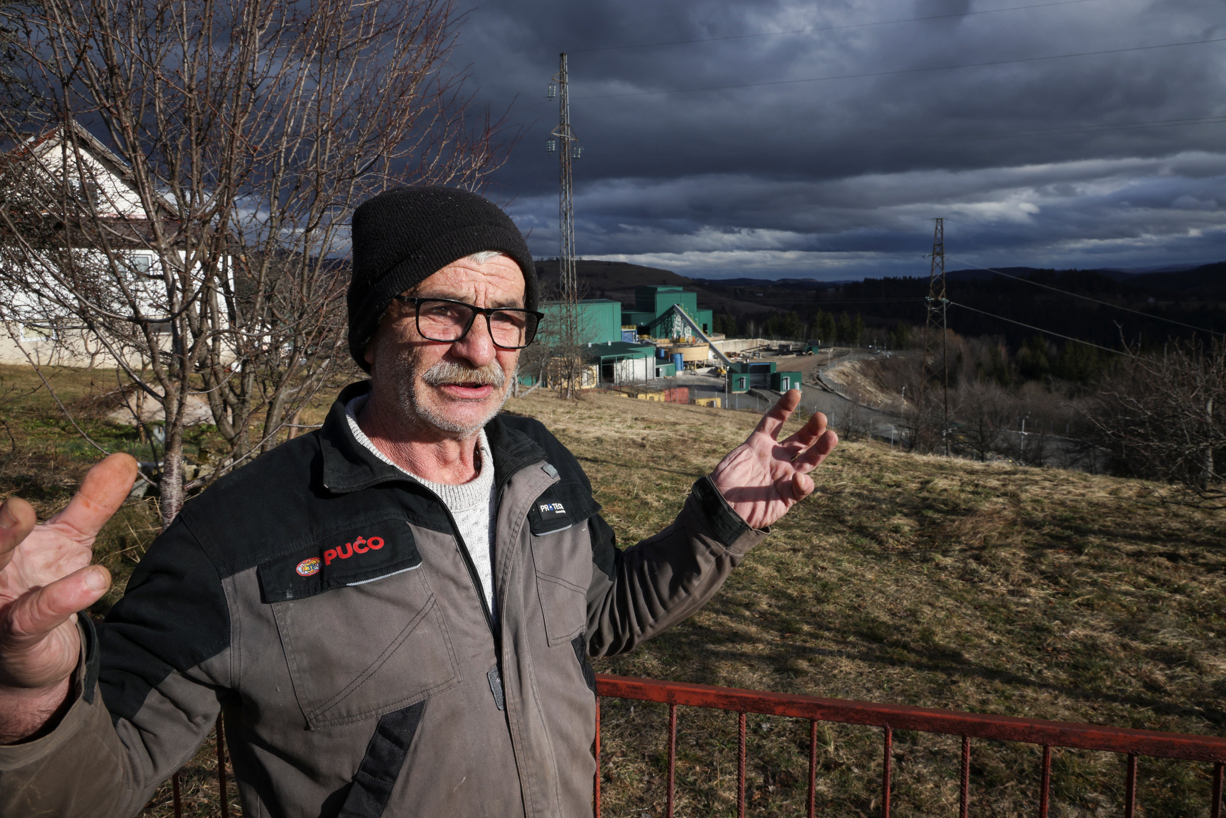 Mladen Zizak gestures as he stands next to a facility of the newly opened silver mine, seen in the background, as concern grows in his community, located near the mine in the village of Tisovci near Vares, Bosnia and Herzegovina,