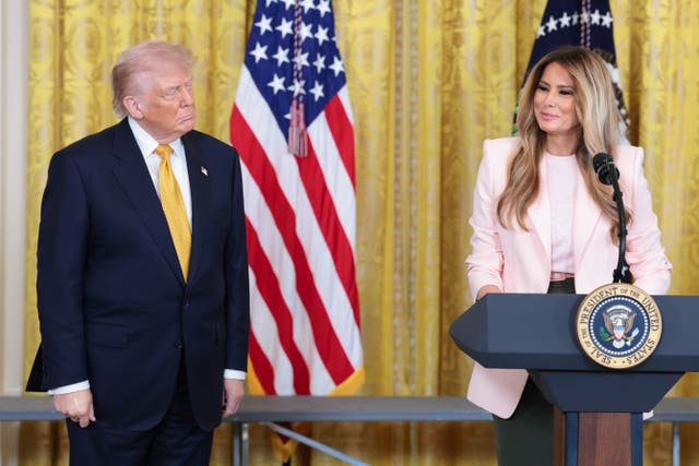President Donald Trump and First Lady Melania Trump at the White House. Melania is speaking at a lectern with the presidential seal