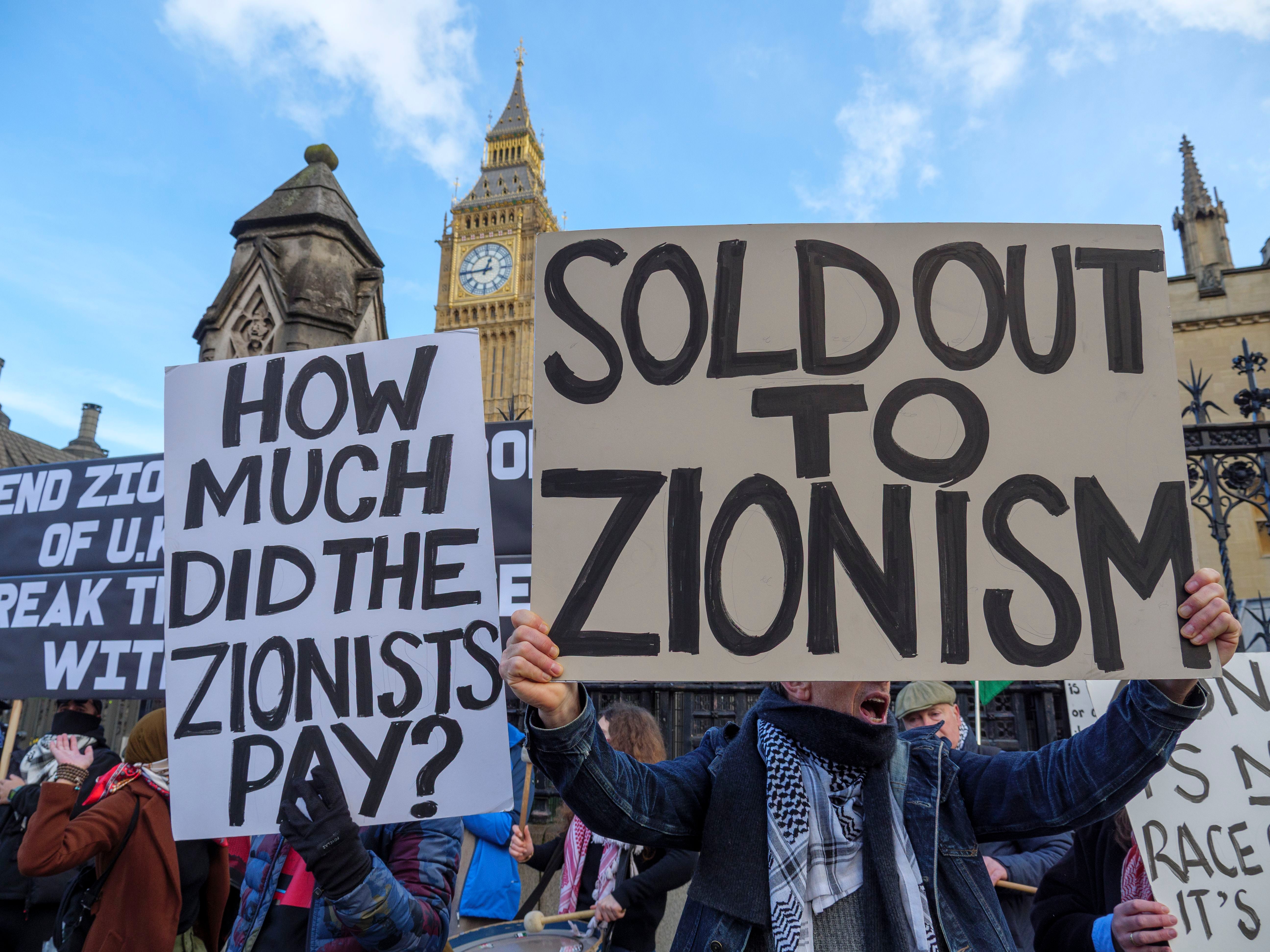 <p>Anti-Zionists holding signs at a protest outside the Houses of Parliament</p>