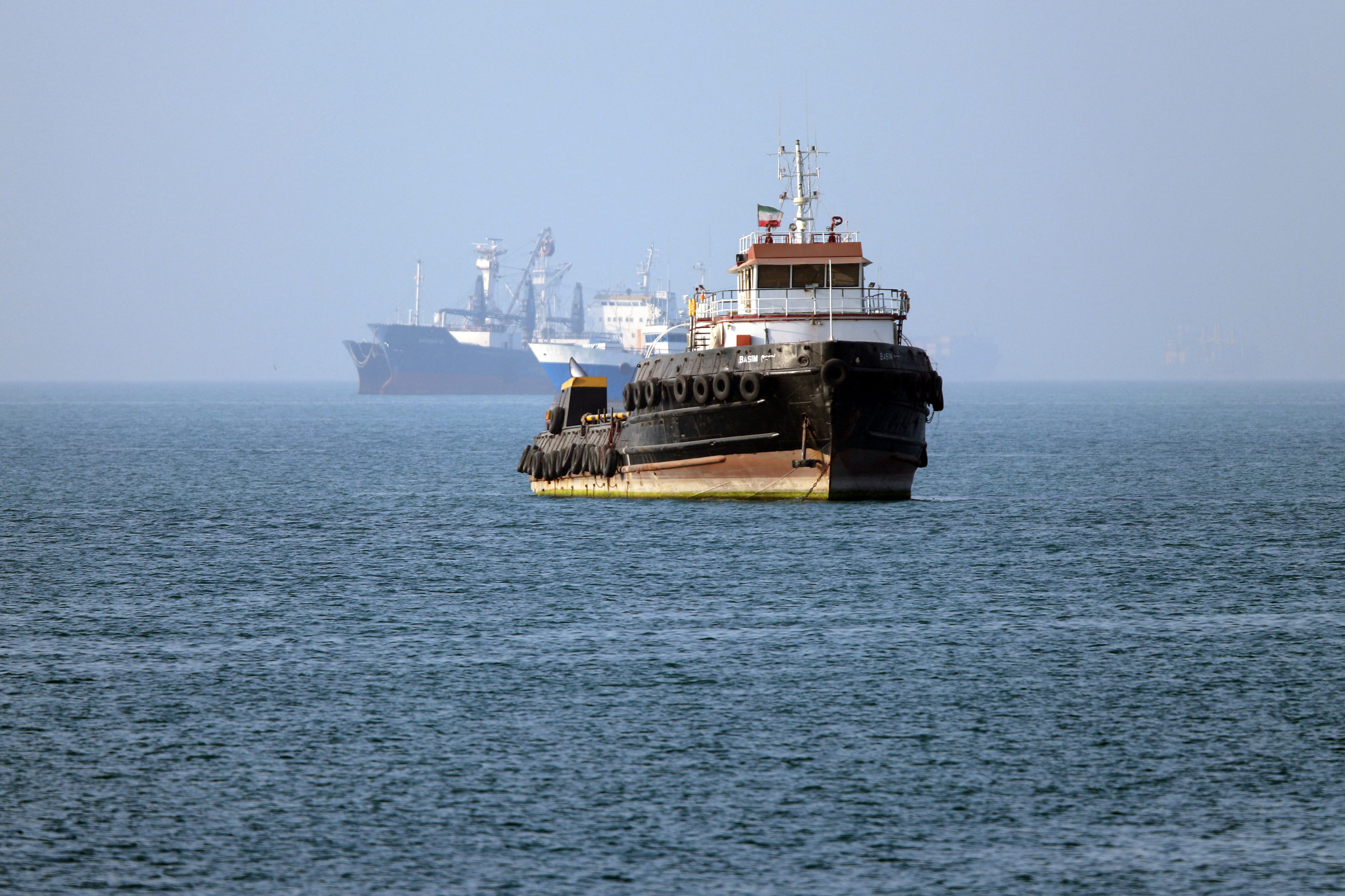 The Iran-flagged tugboat Basim sails near a ship anchored in the Strait of Hormuz off Bandar Abbas