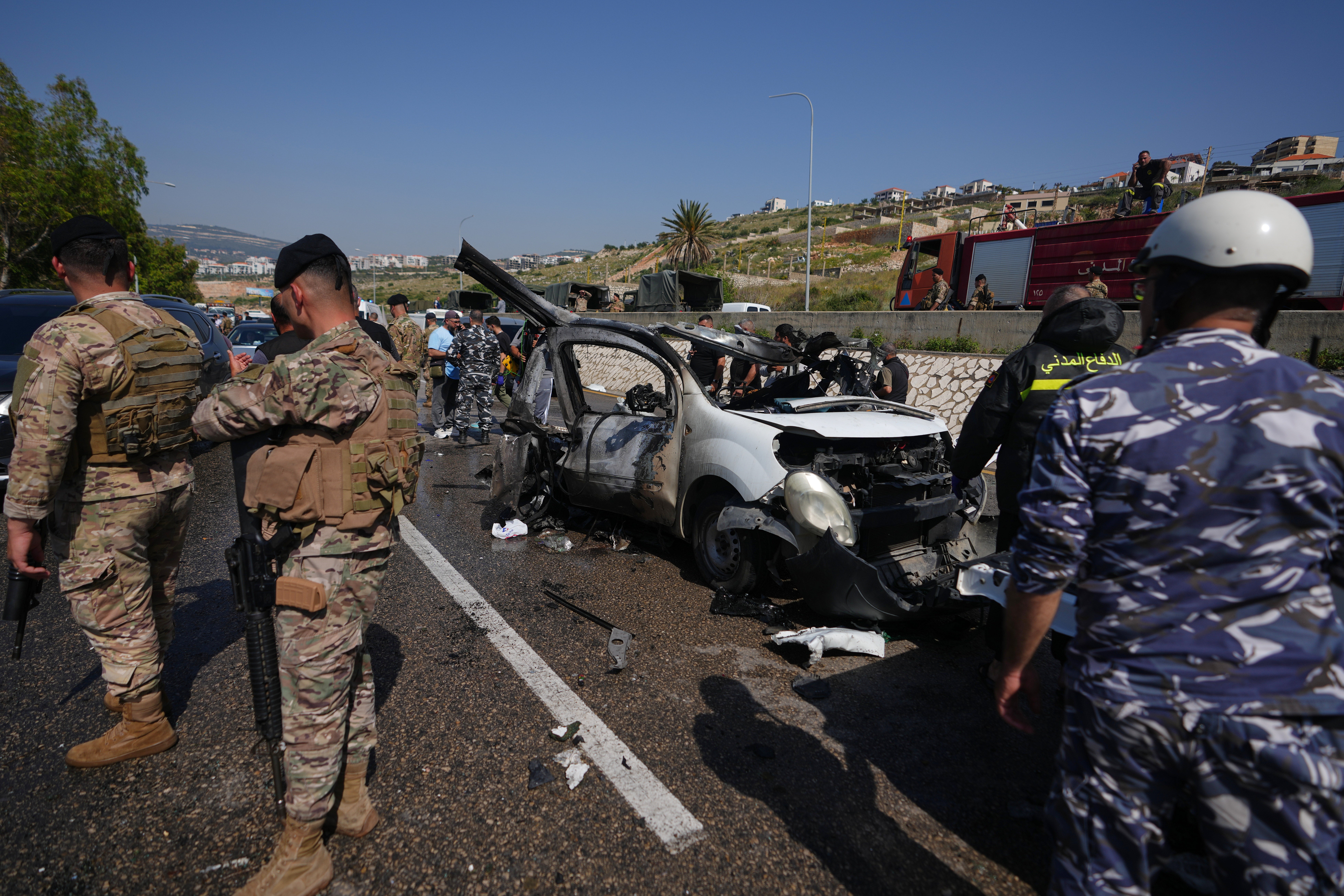 Security forces and emergency responders gather around a damaged vehicle at the scene of an Israeli airstrike that hit a car in the coastal town of Saadiyat, south of Beirut