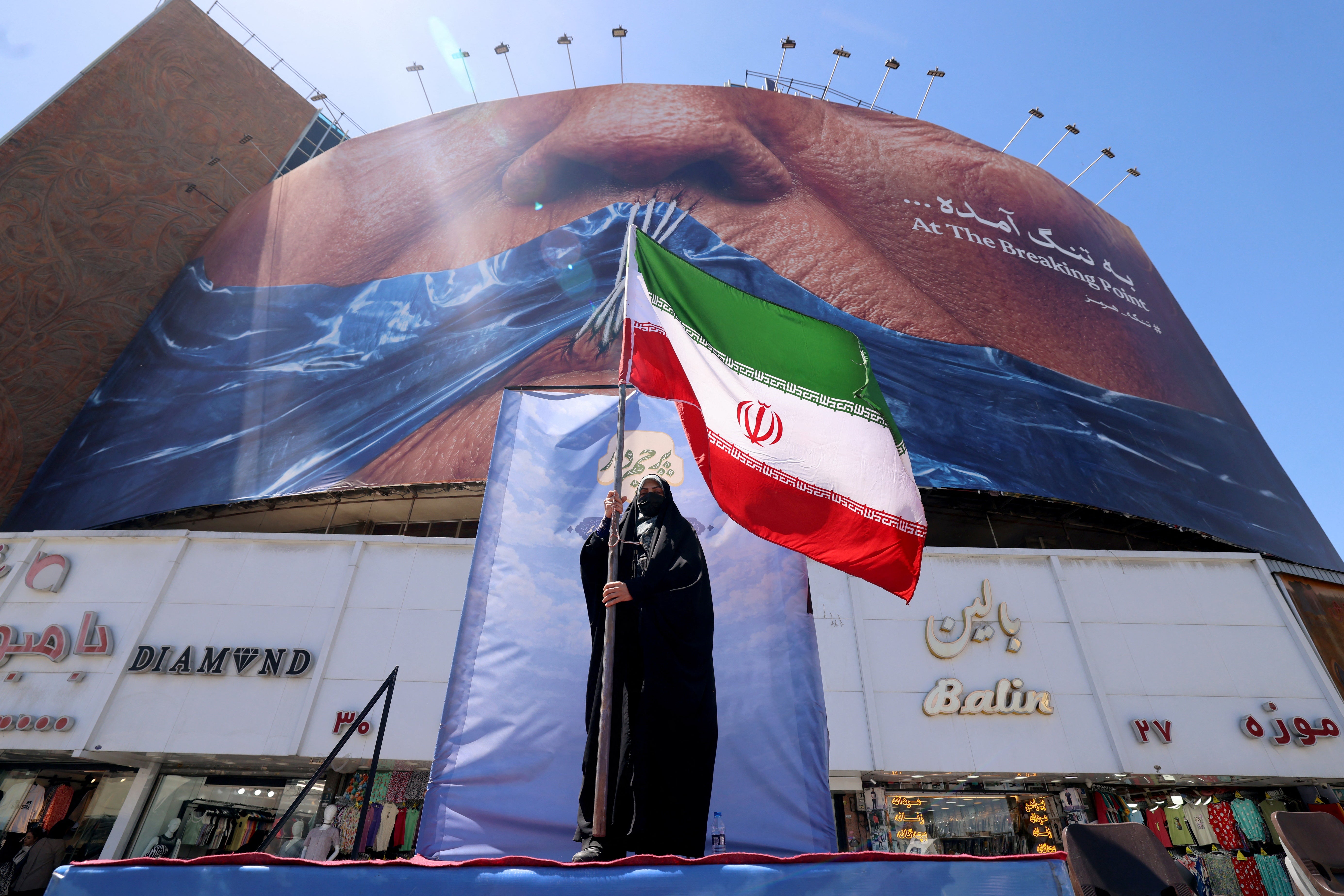 A woman holds the Iranian flag as she stands infront of an anti-US billboard referring to President Donald Trump and the Strait of Hormuz, installed on a building at the Valiasr Square in Tehran