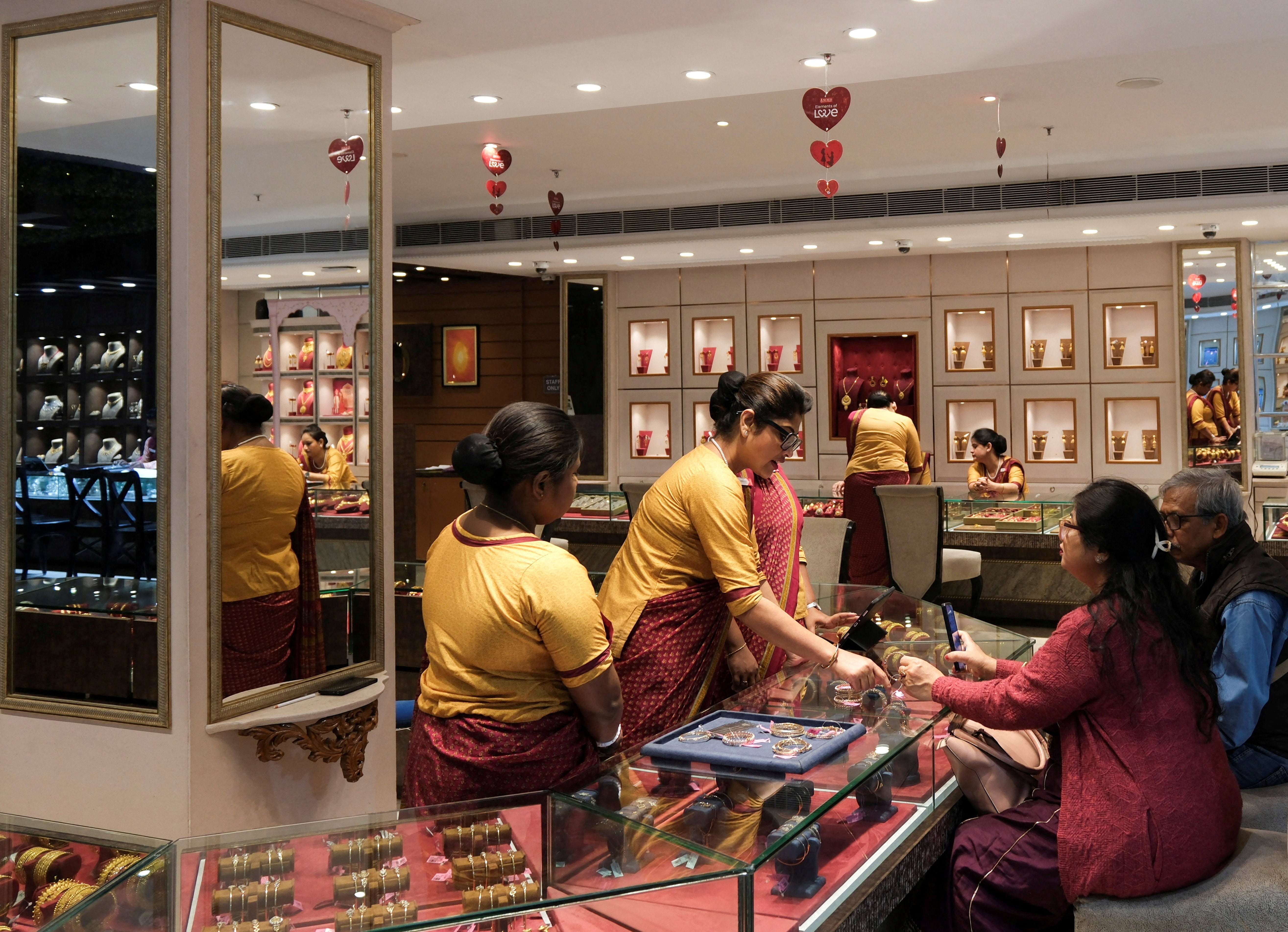 Saleswomen show gold ornaments and jewellery to customers for purchase inside a jewellery showroom in Kolkata, India