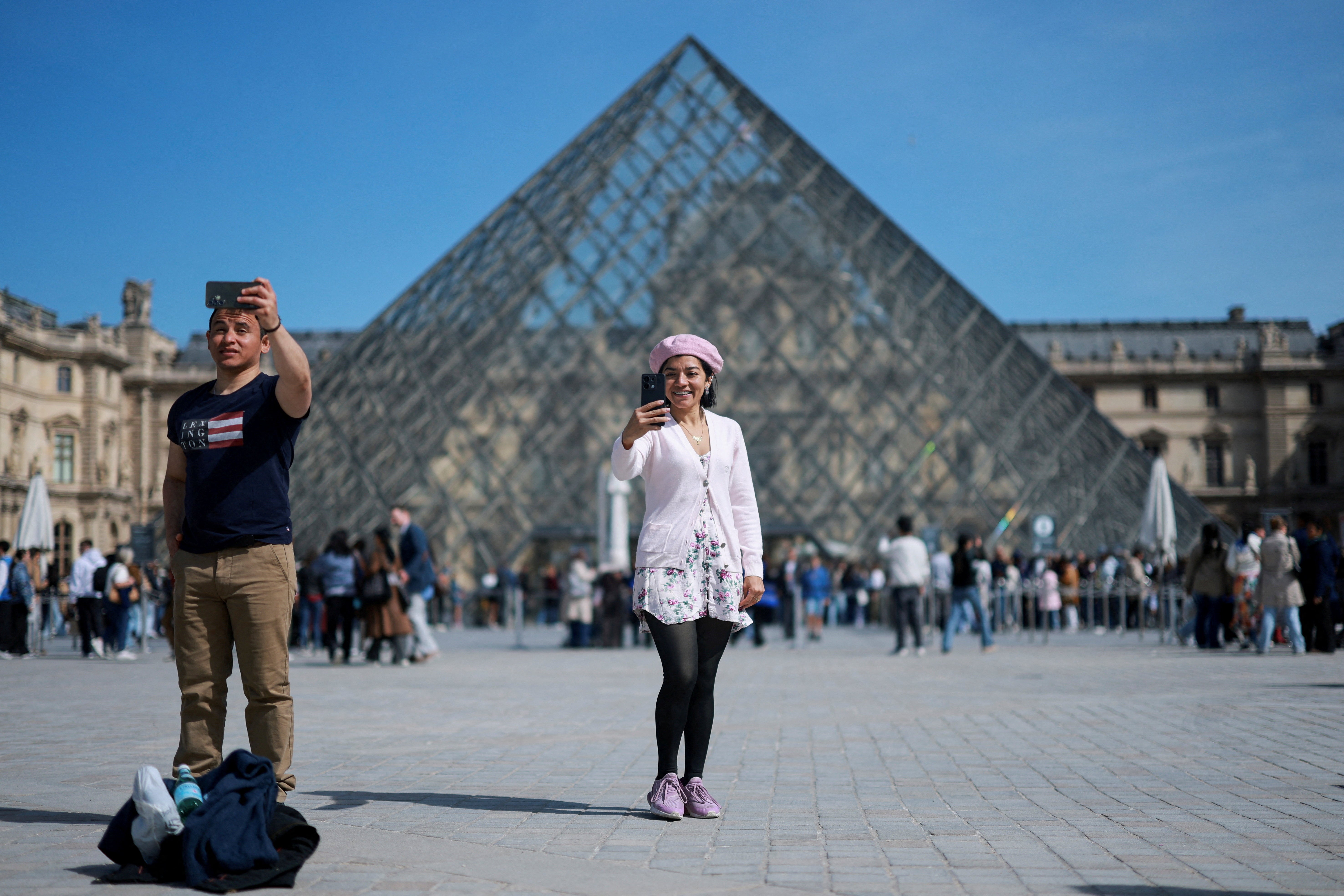 Tourists take selfies in front of the glass Pyramid of the Louvre museum