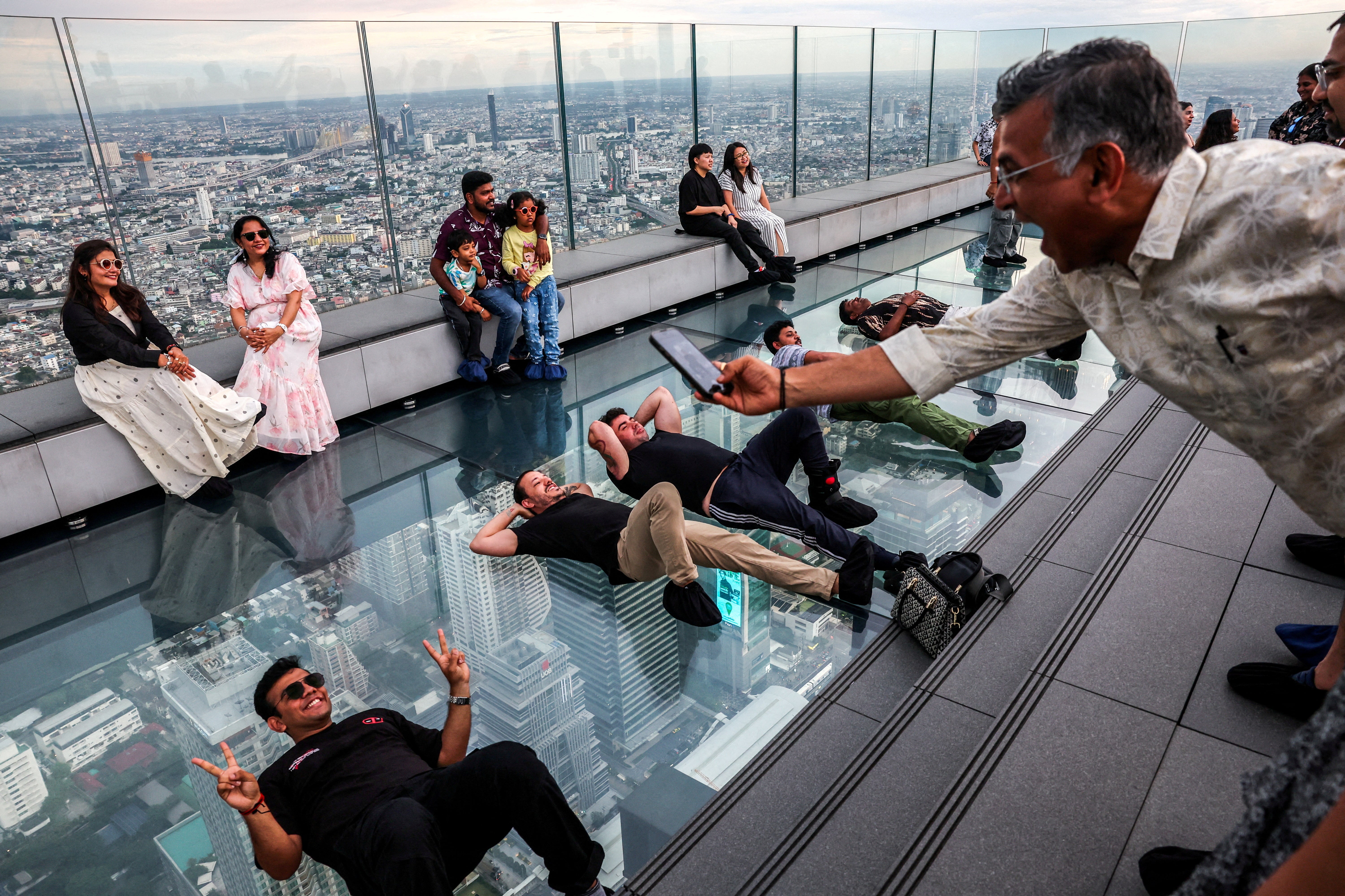 Tourists pose as they enjoy the Mahanakhon Skywalk Rooftop at Mahanakhon building in Bangkok, Thailand