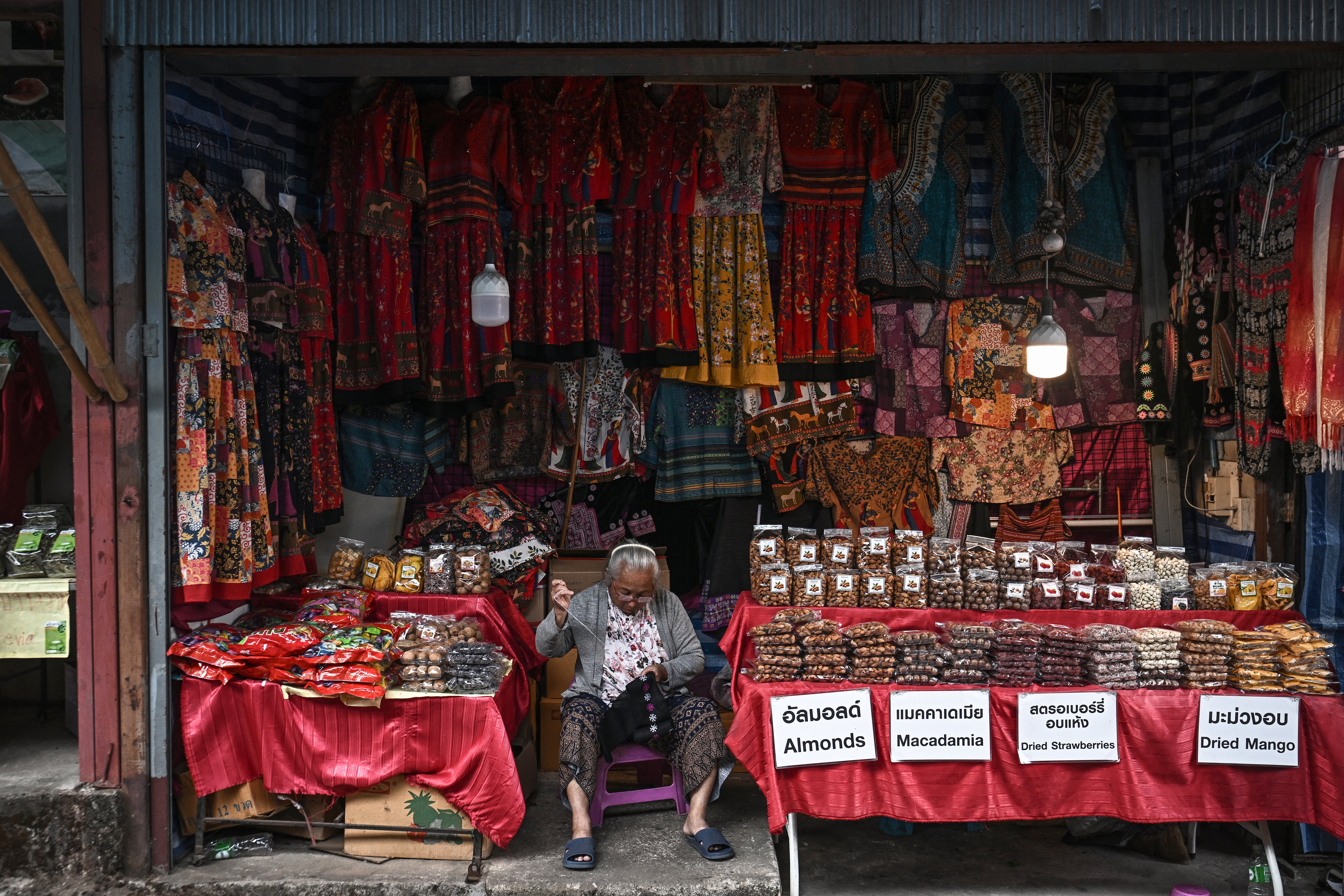 Hmong vendor sewing clothing at a stall selling souvenirs for tourists in the Hmong Doi Pui Village in the Doi Suthep-Pui National Park area of Chiang Mai